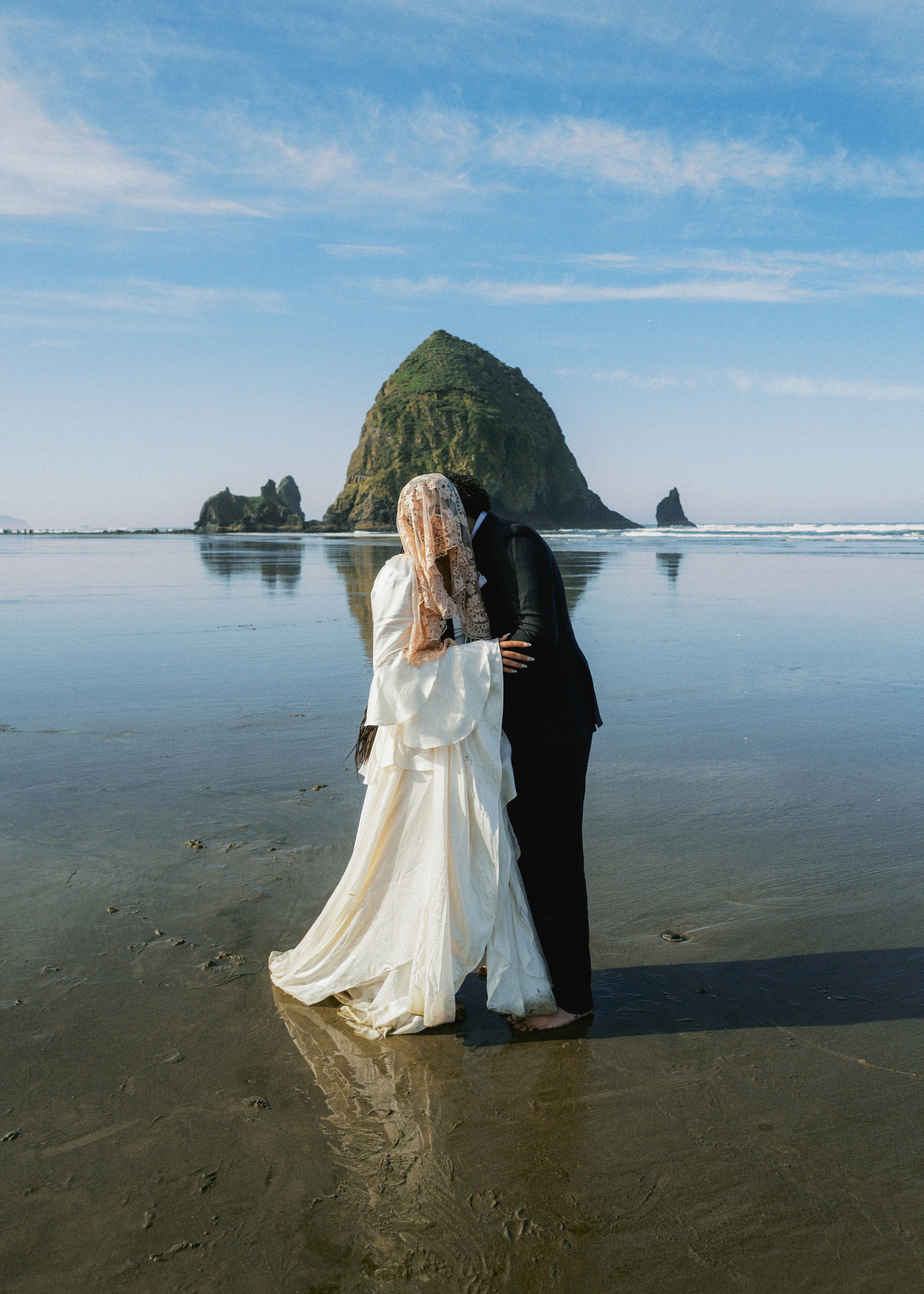a bride and groom embracing on cannon beach at sunrise