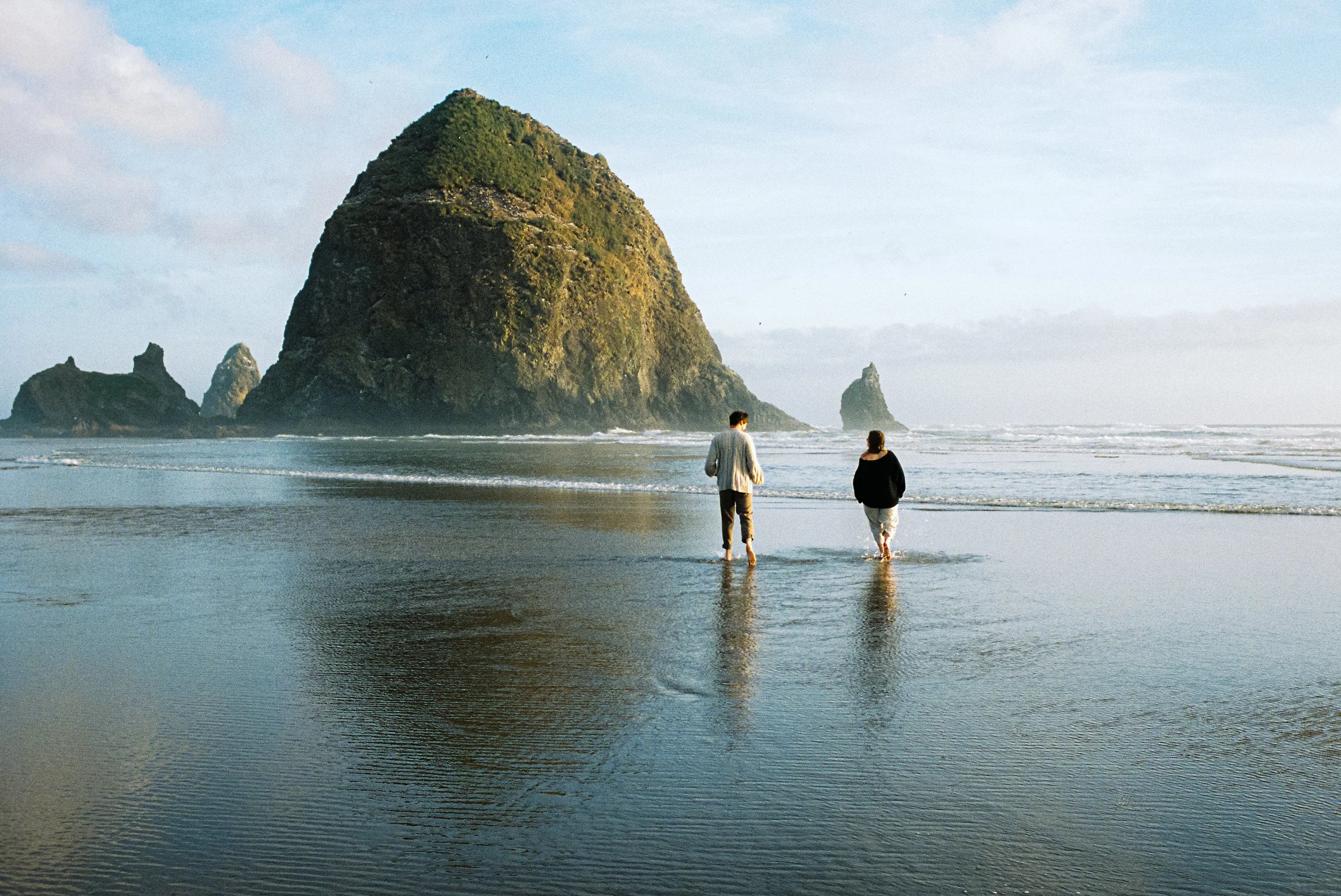 a couple running away into the ocean with Haystack Rock at Cannon Beach in the background