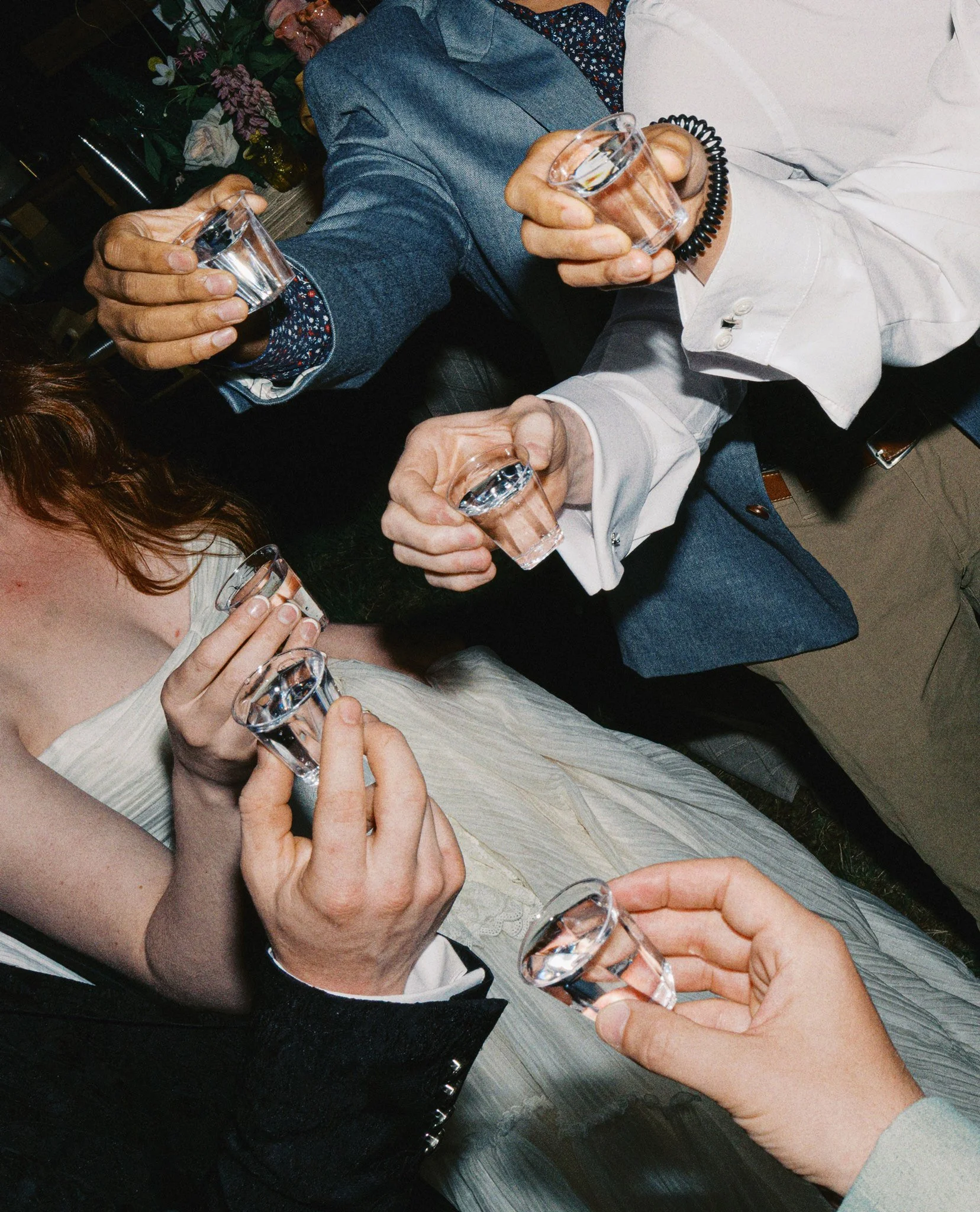 Several people holding small shot glasses filled with clear liquid, gathered around a table, suggesting a social toast or celebration.