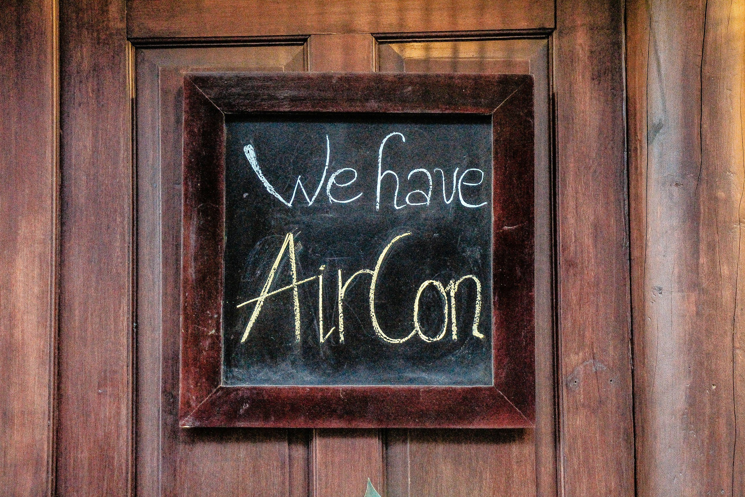 A small black chalkboard with a wooden frame, hanging on a wooden wall, displaying the words 'We have Airdon' written in white and yellow chalk.