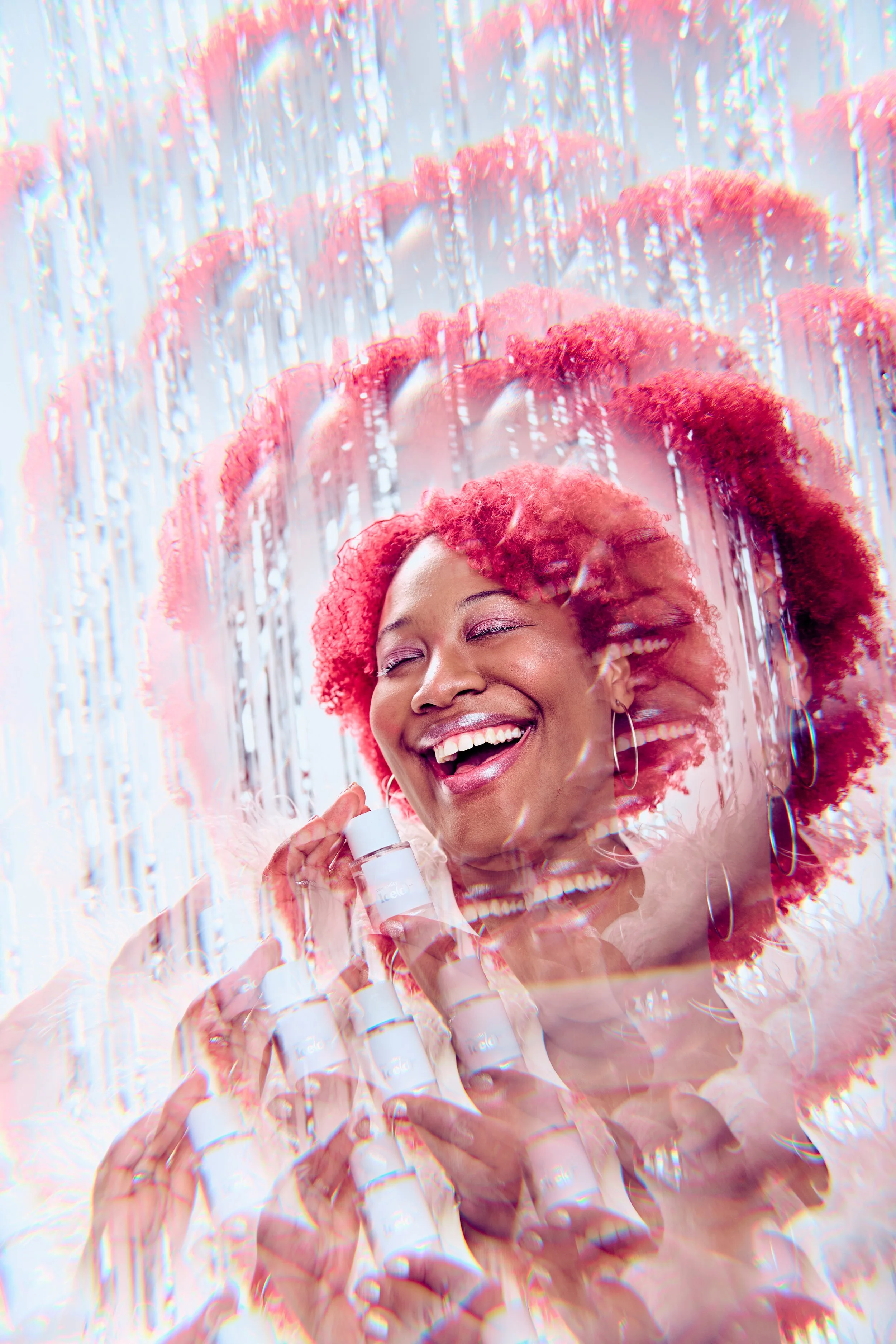 A woman with red curly hair smiling with closed eyes while holding skincare products, surrounded by a layered, distorted visual effect.