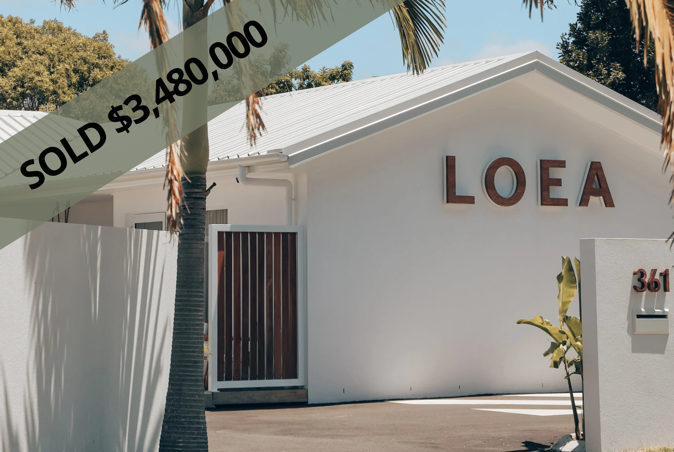 Modern white motel with a sign reading 'LOEA' on the front wall and house number 361 on a white wall with a mailbox, palm trees, and a clear blue sky.