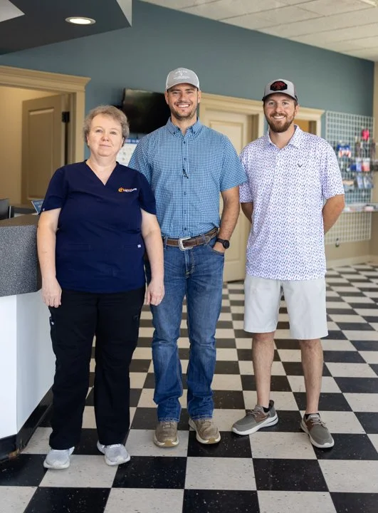 Three people standing inside a retail store with checkered black and white floor, shelving unit and a counter in the background.