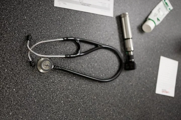 A stethoscope, flashlight, medicated cream tube, and a handwritten note on a dark surface, likely part of a medical or health-related setting.