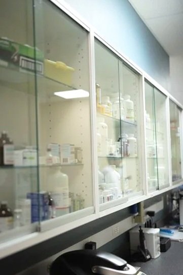 Glass pharmacy cabinet filled with medication bottles and boxes.