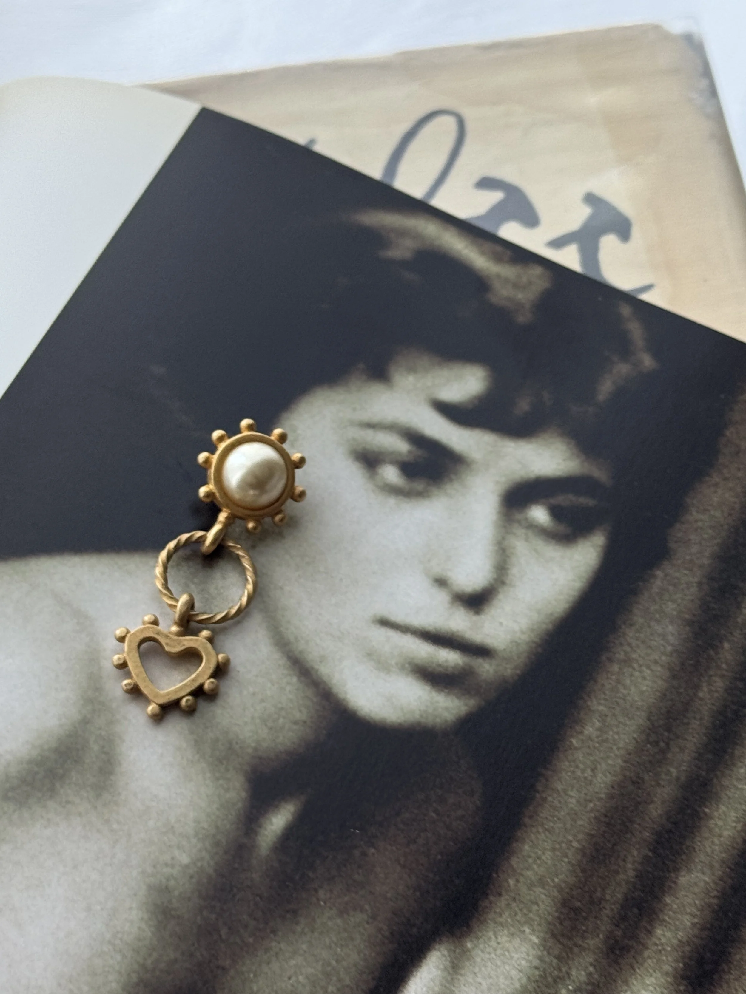 Black and white photograph of a young woman with ponytail, smiling softly, with a gold and pearl charm pin placed on her shoulder. nude art photography