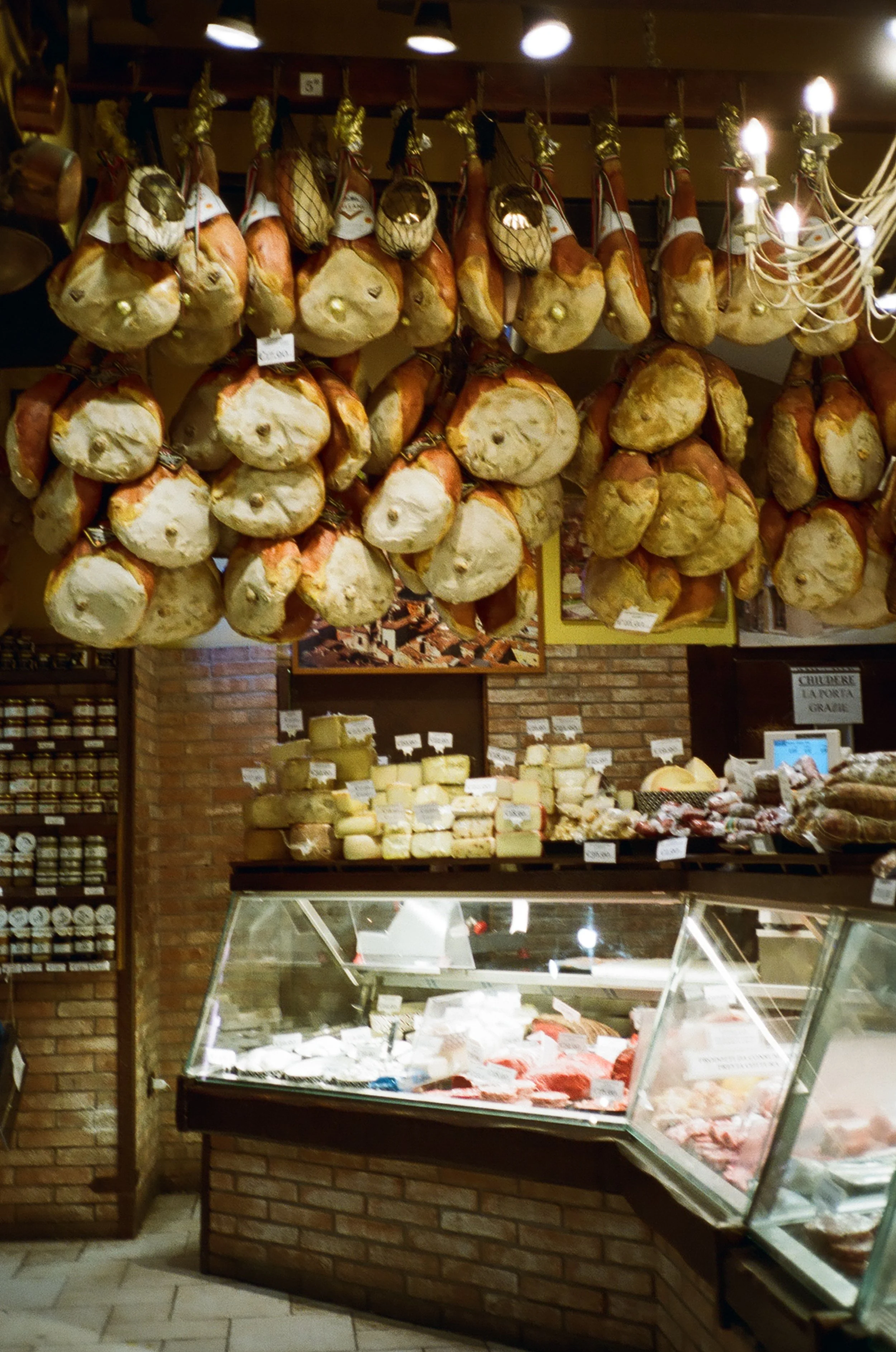 Dried hams hanging from the ceiling above a cheese and meat shop display case.