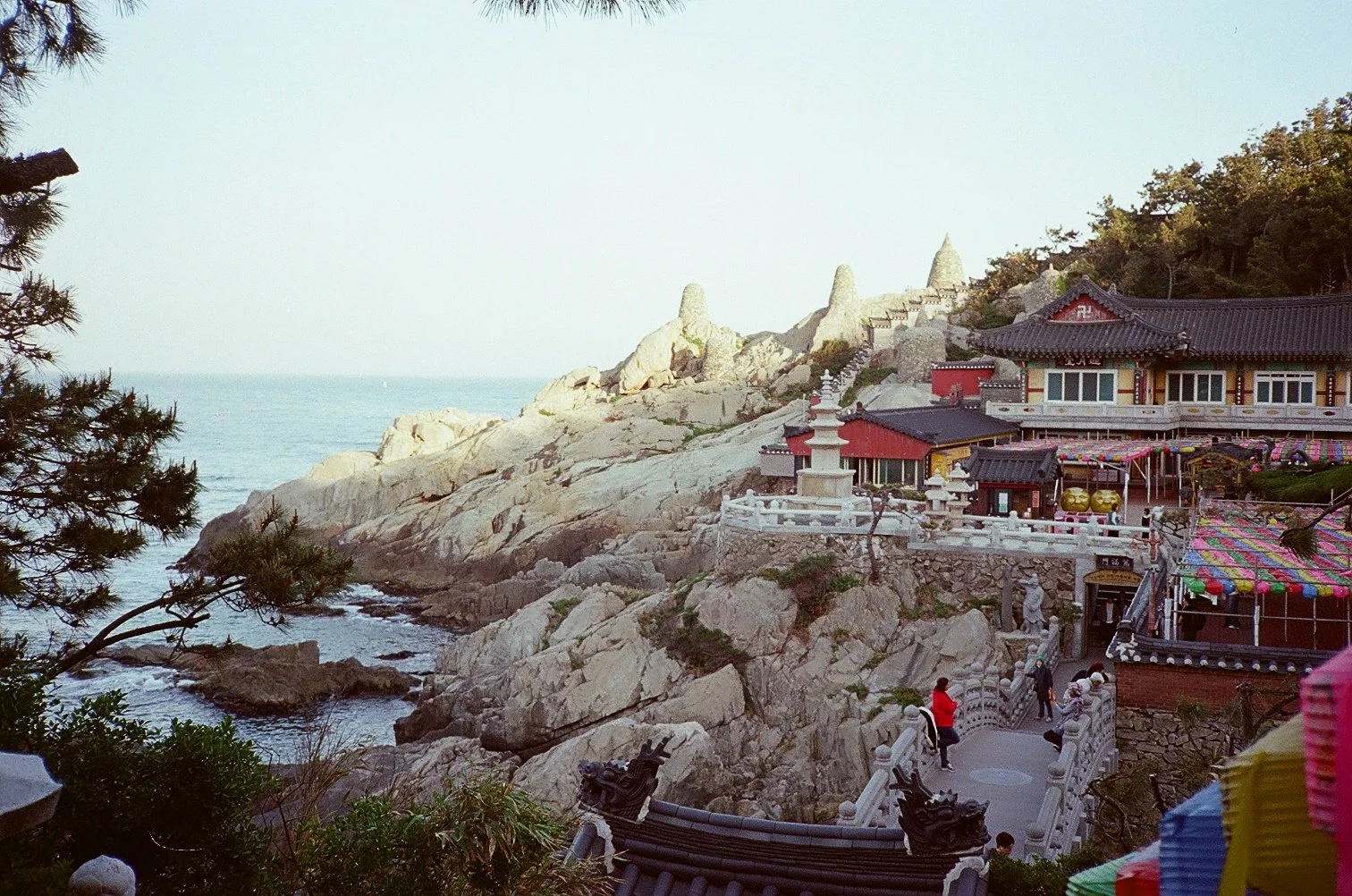 A coastal temple with traditional East Asian architecture, colorful decorations, and rocky cliffs by the ocean.