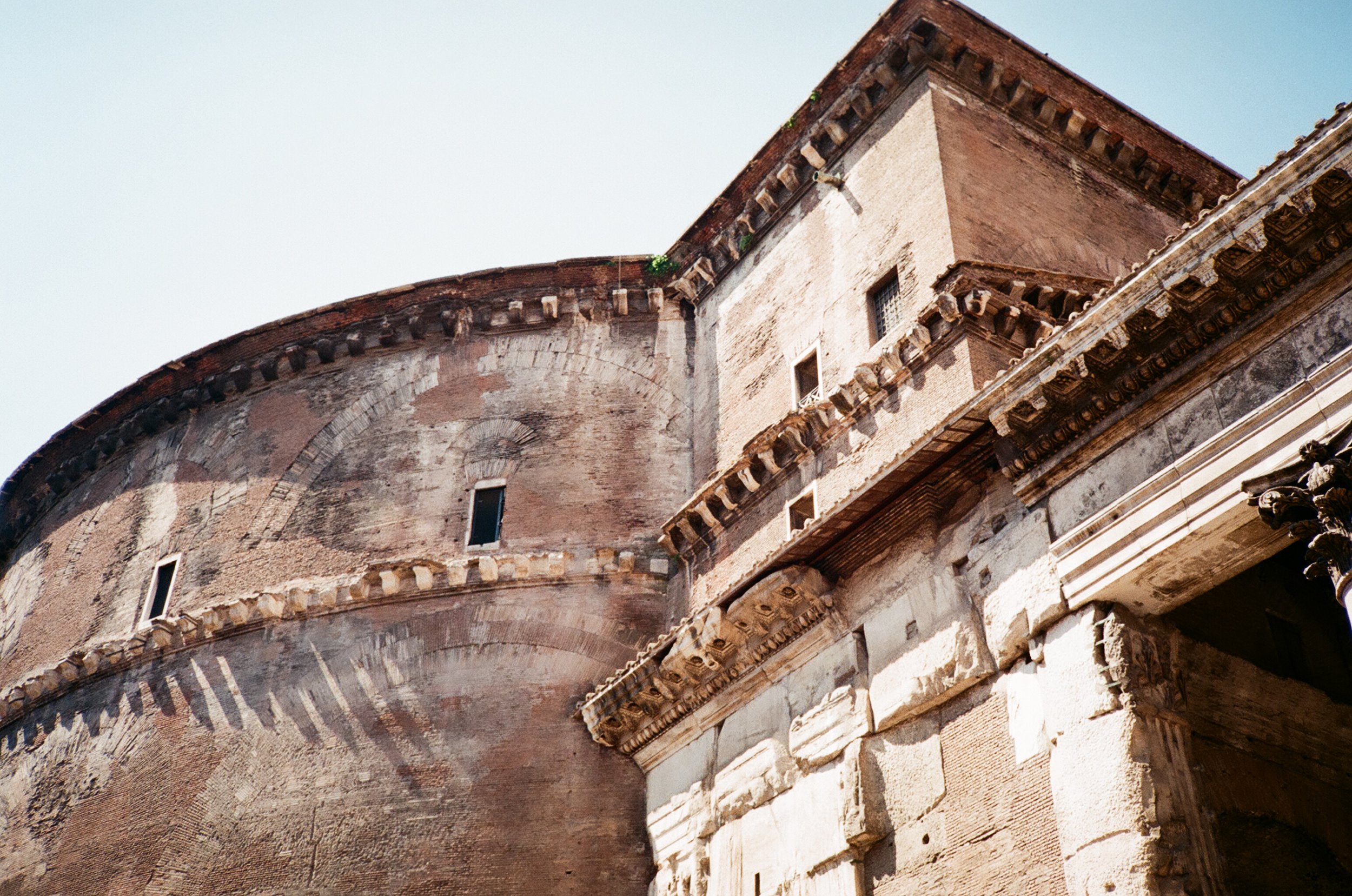 Close-up of ancient Roman architecture showing brick and stone walls with decorative cornices and small windows, part of a historic Roman structure.