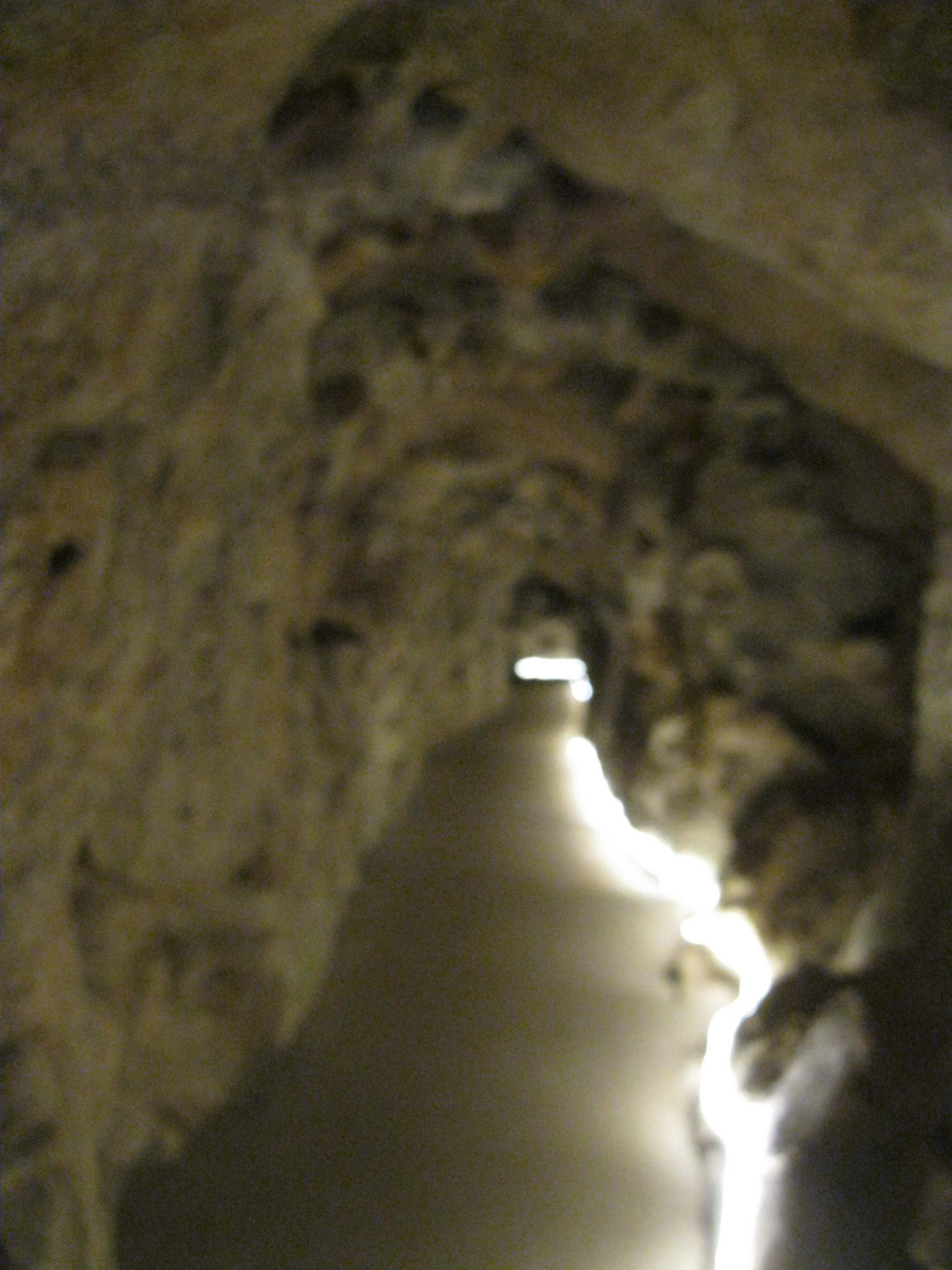Inside a dark cave with rough stone walls and a narrow passage illuminated by light at the end.