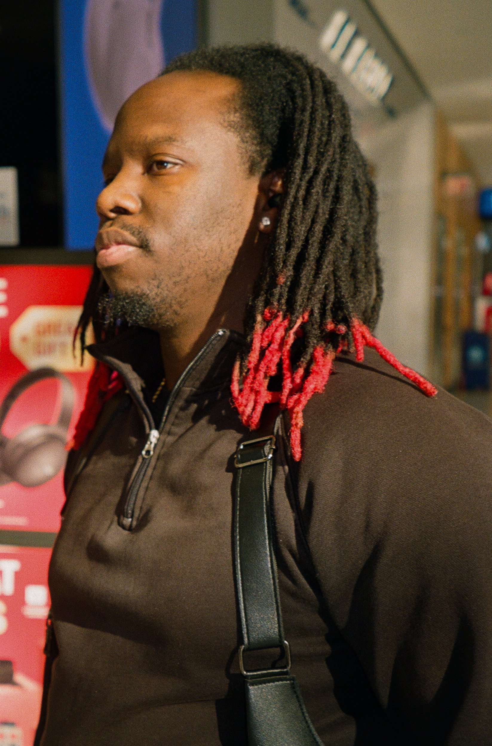 A man with long dreadlocks with red tips standing in front of a red vending machine.