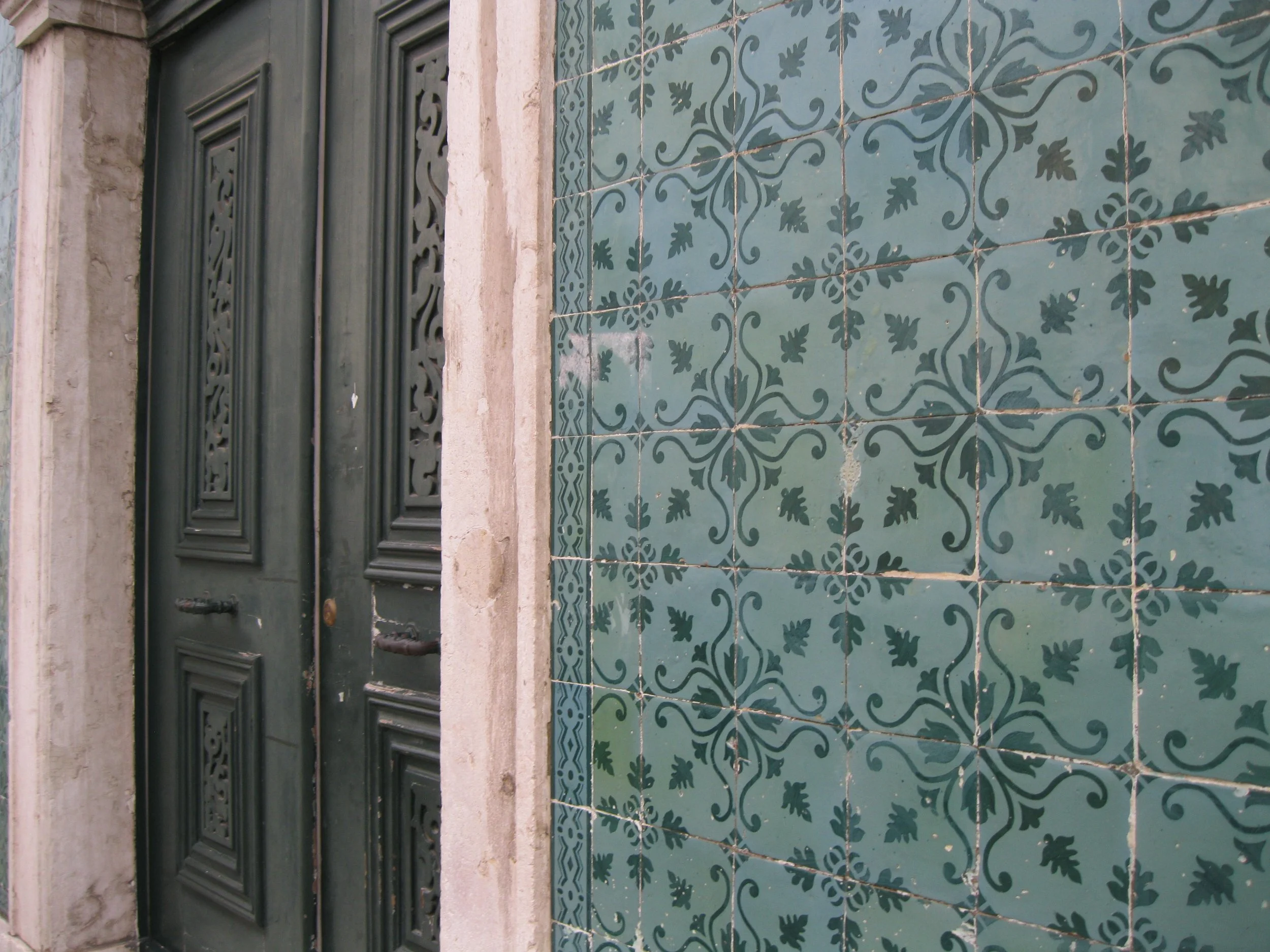 A green wooden door with ornate carvings next to a wall of decorative blue and green patterned tiles.