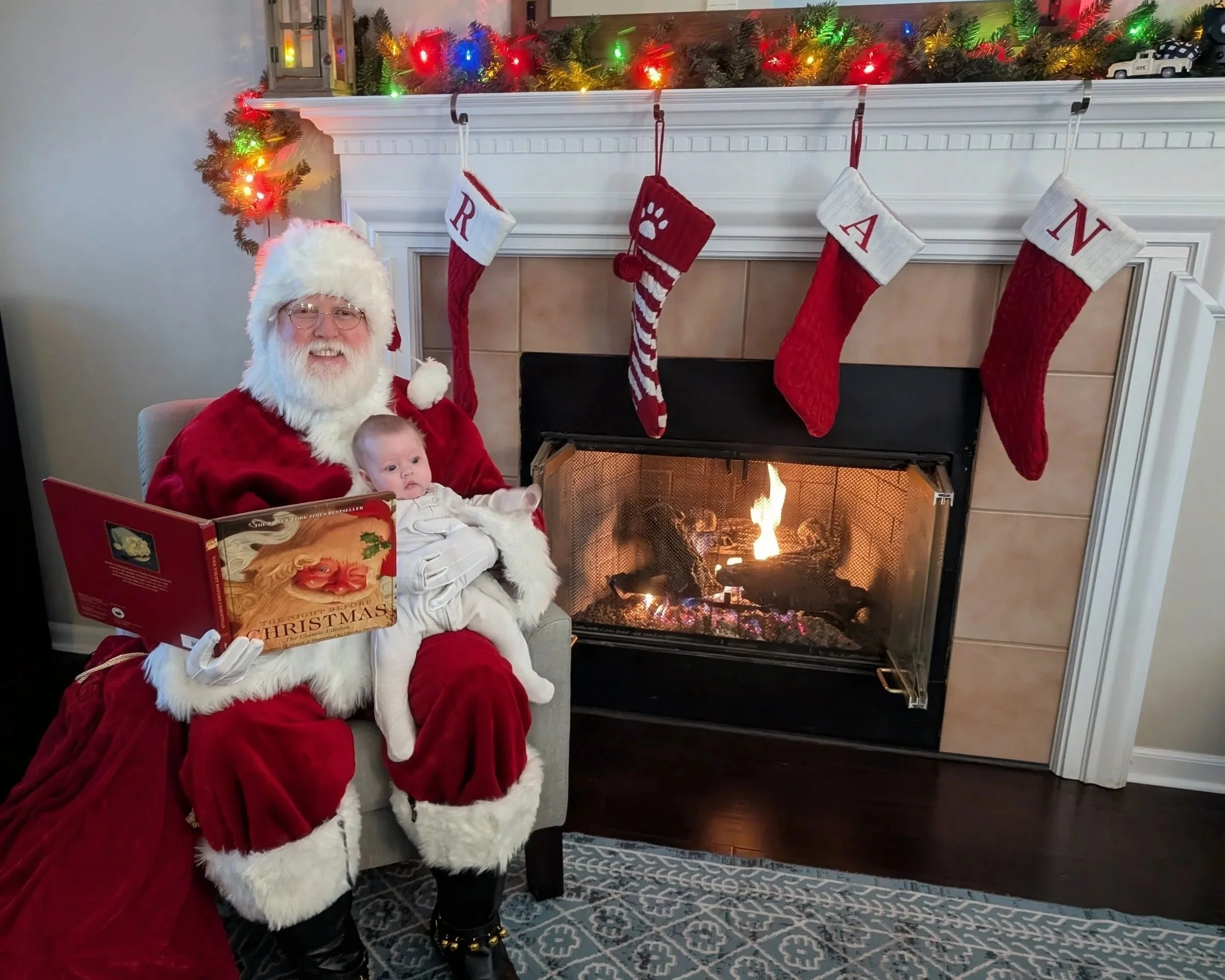 Santa Snow sits by the fire reading a book to a baby on his knee.