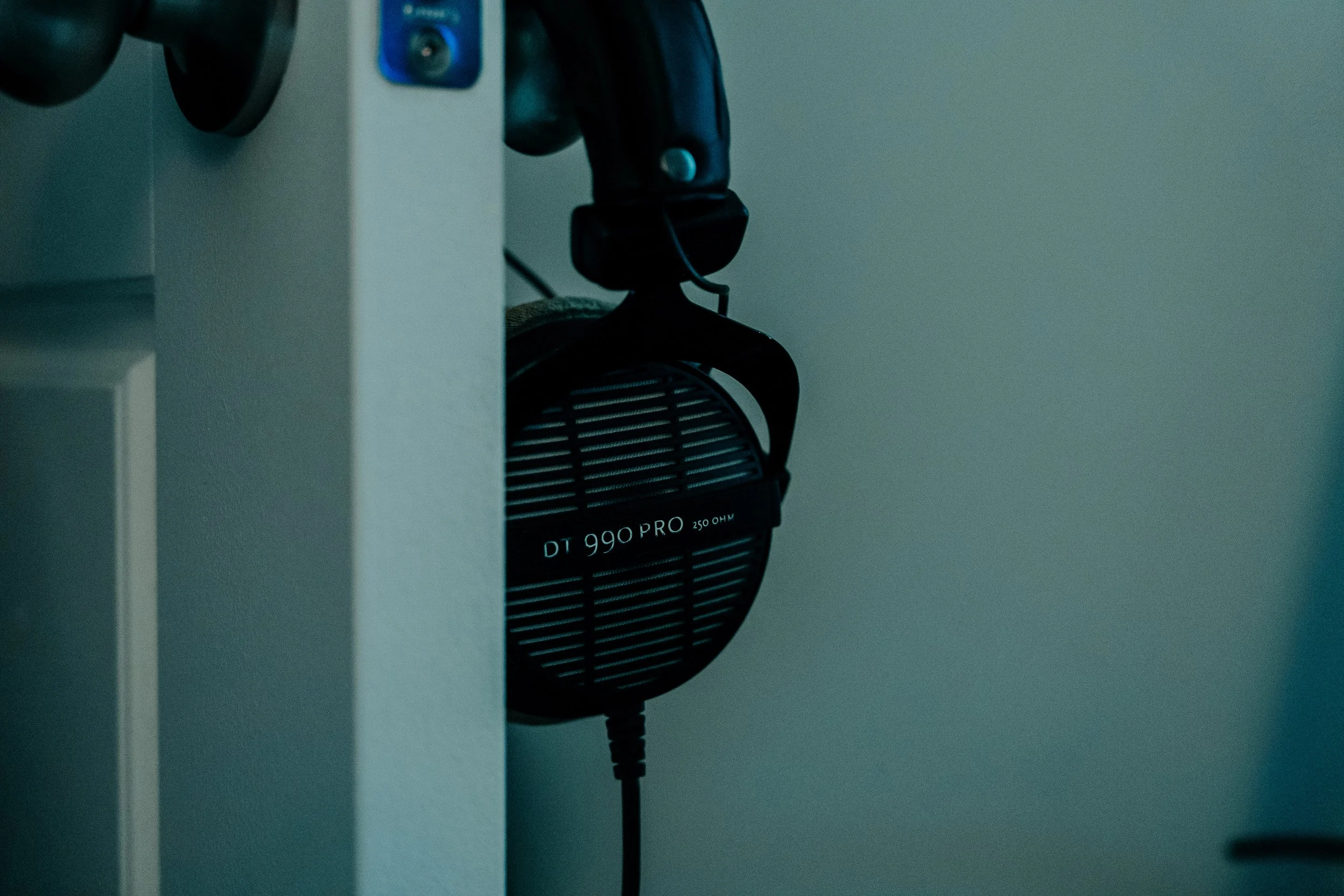 A pair of black Beyerdynamic DT 990 PRO headphones hanging on a wall hook with a gray wall in the background.
