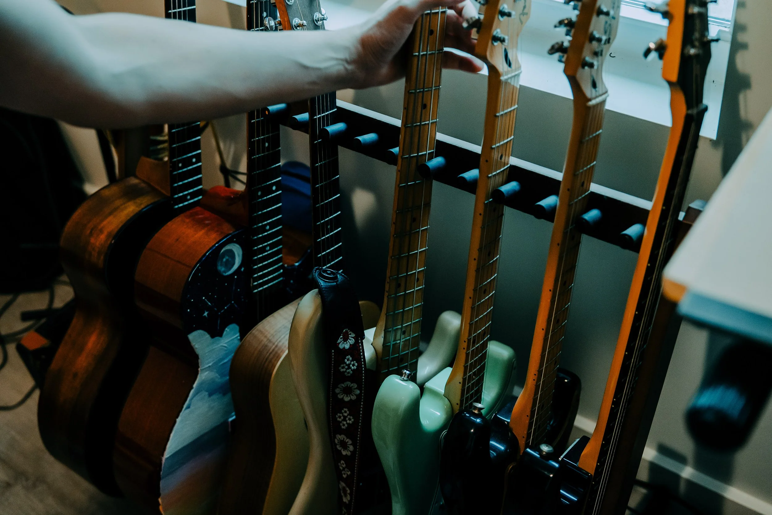 Collection of guitars placed vertically in a storage rack, including acoustic and electric guitars in various colors and finishes.