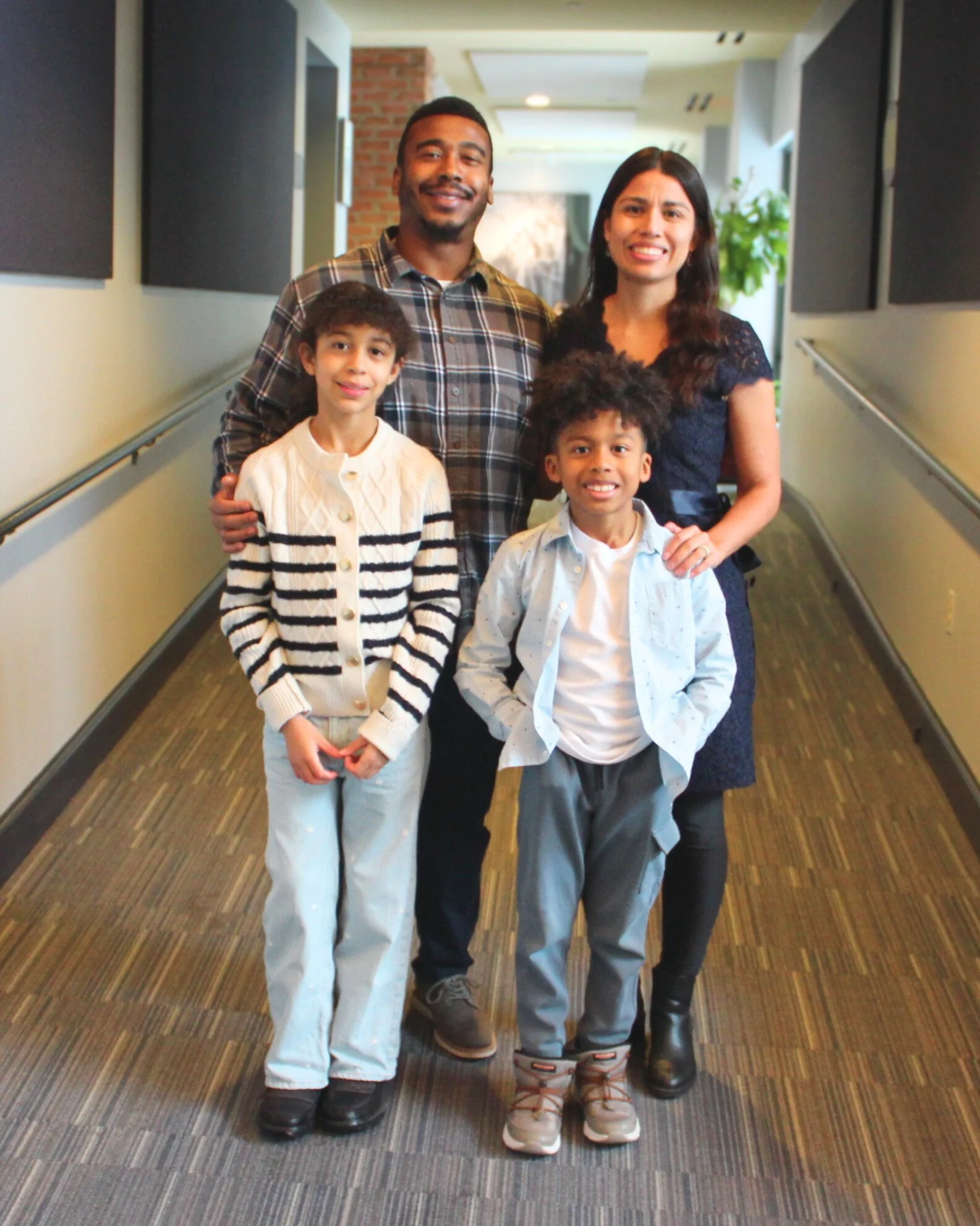 A diverse family of four in a hallway, smiling at the camera.