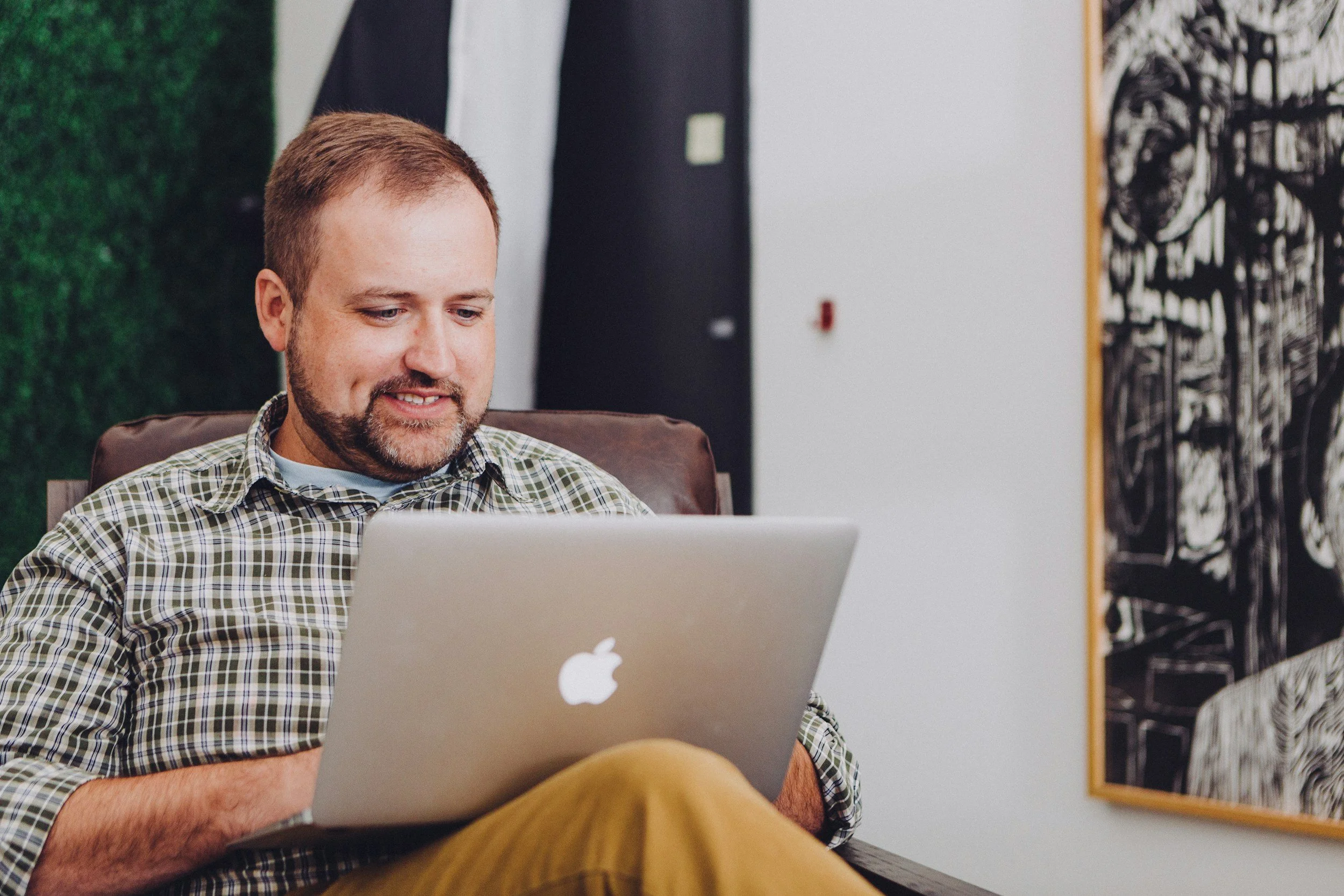 Man sitting on a chair using a MacBook in an office setting.
