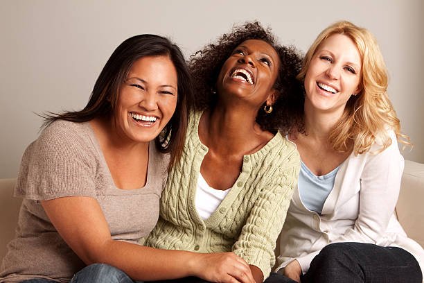 Three women sitting close together on a sofa, laughing and smiling.