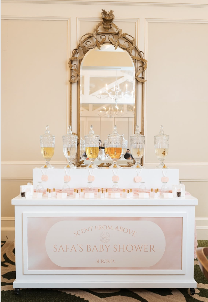 A reception table at a baby shower themed 'Scent from Above,' with glass dispensers of beverages, a mirror above, and a sign indicating it's a baby shower for Safo.