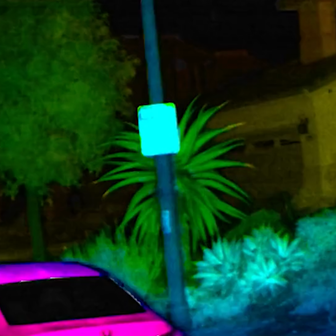 Nighttime scene with a pink car, a blue-lit sign on a pole, and green plants in the background.