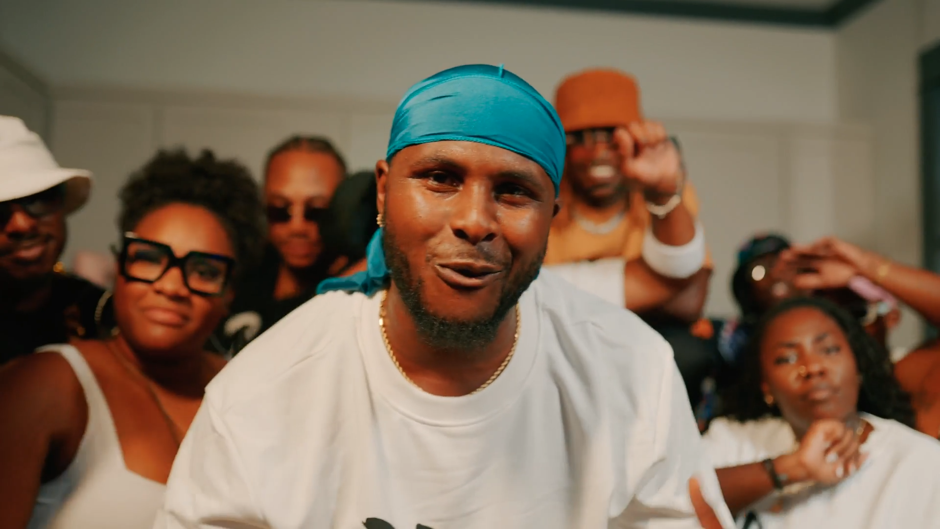 A group of diverse people gathered together, with some smiling and others appearing surprised or thoughtful, in an indoor setting.