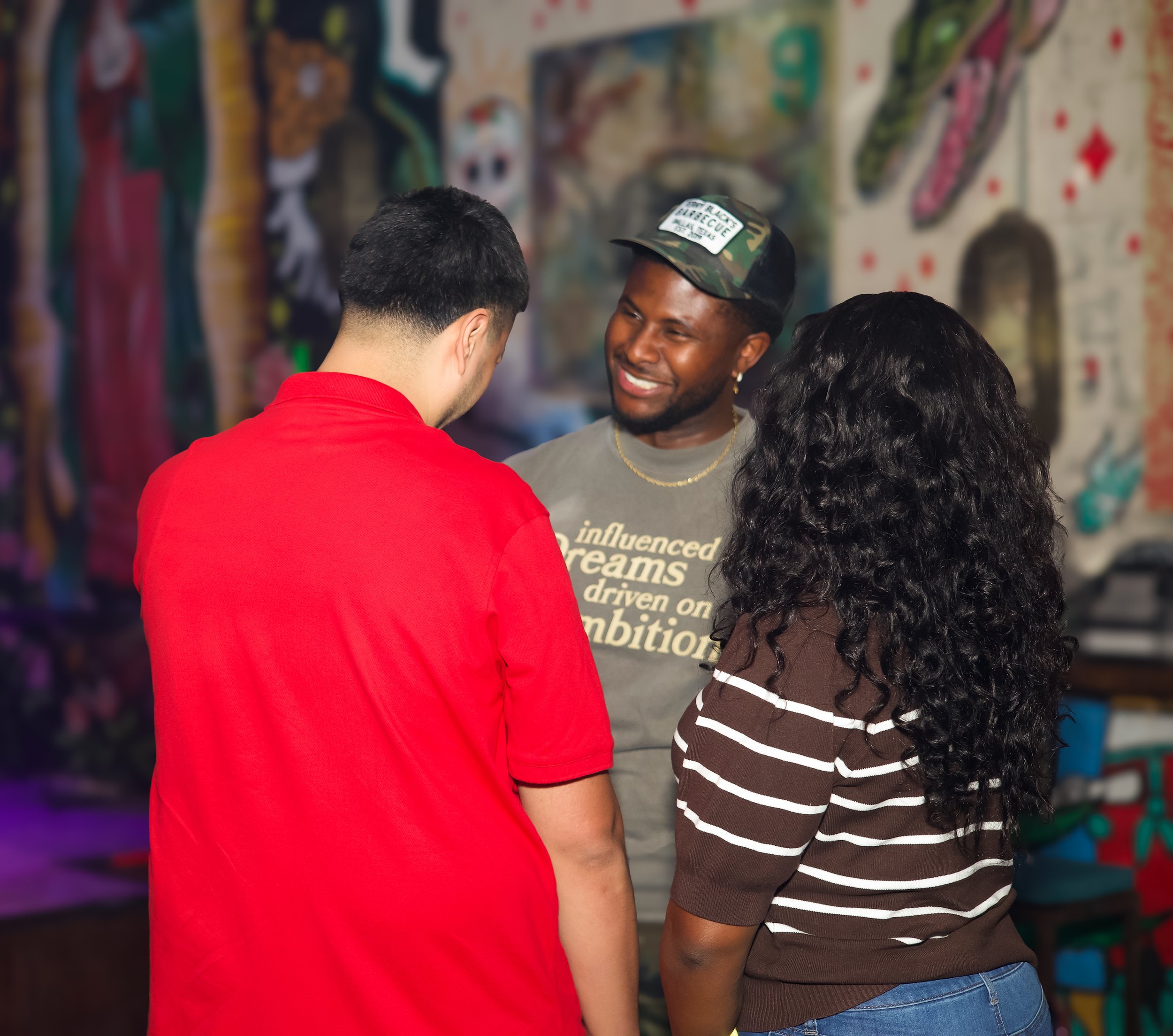 Three people having a conversation indoors, with a colorful mural in the background.