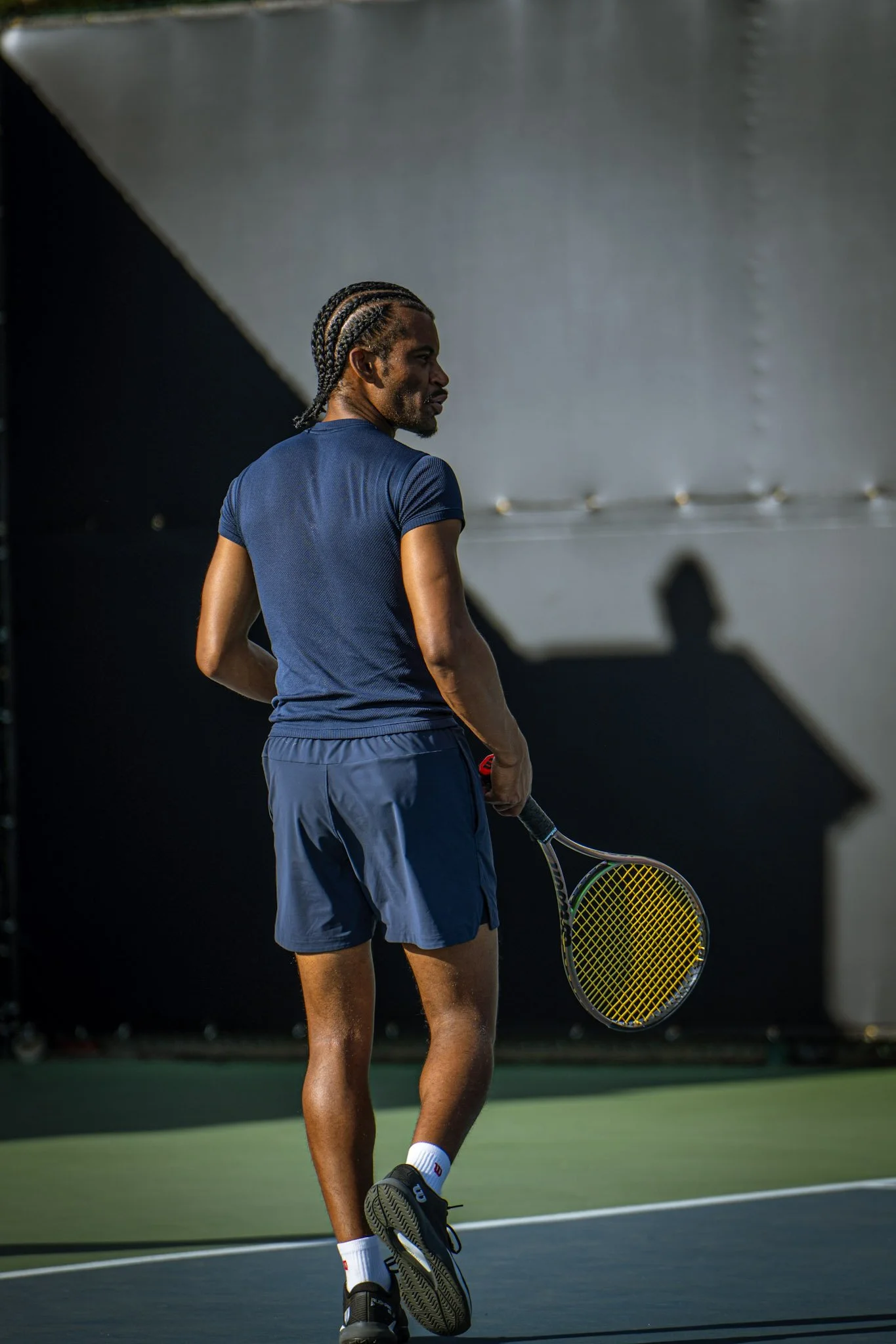 A man with braided hair holding a tennis racket on a tennis court.