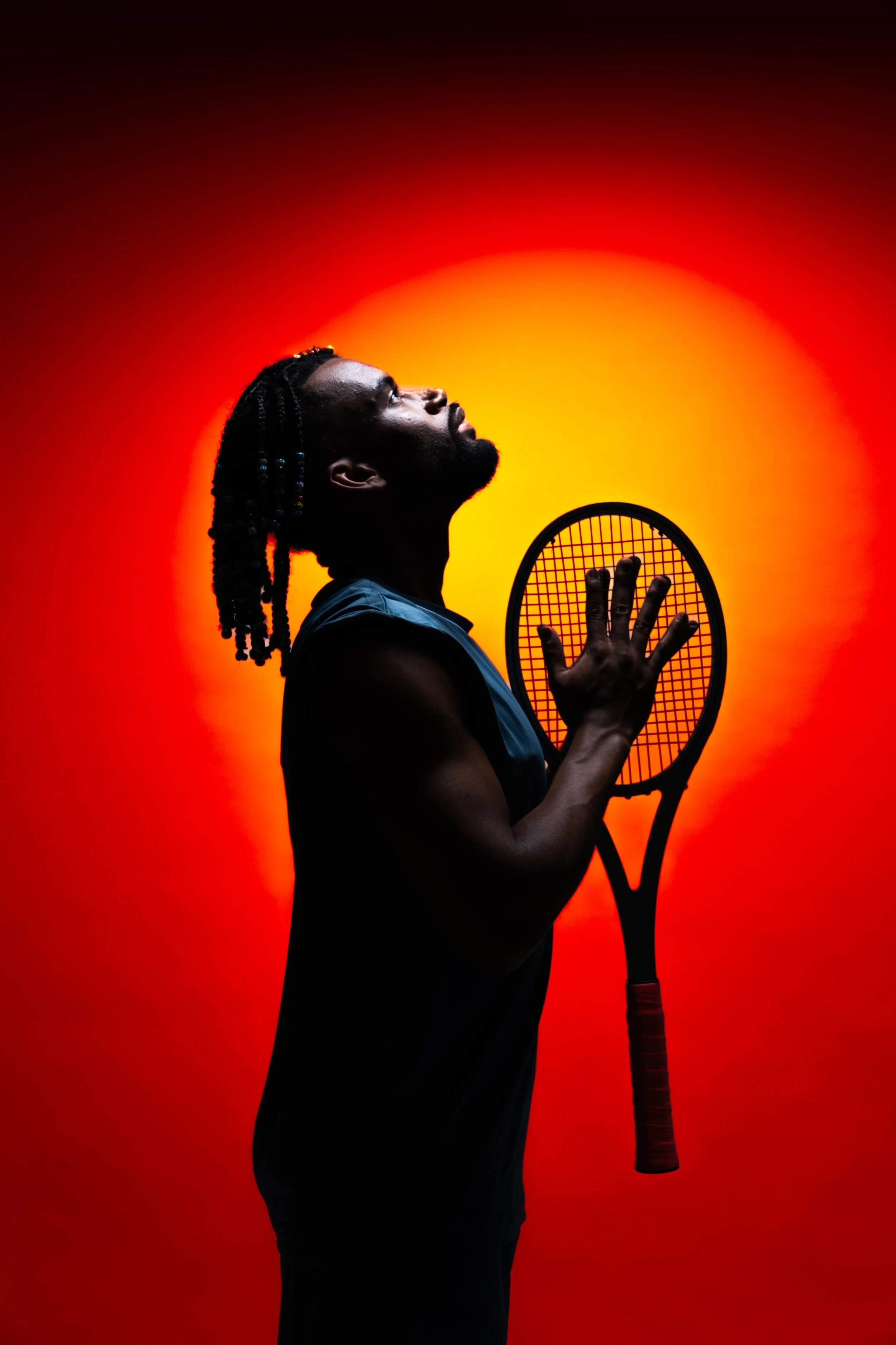 A silhouetted man with braided hair holding a tennis racket, standing against a vibrant red and yellow gradient background.