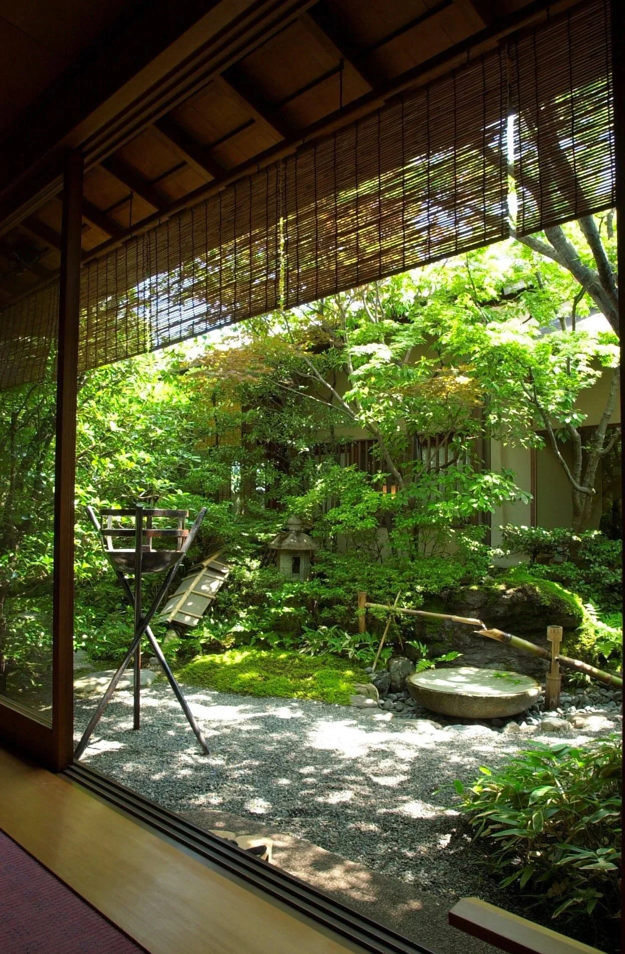 悟道庵点景 | 室内から庭を眺める。苔と植物に覆われた地面、石灯籠や水車、梅の木が見える。木陰に光が差し込み、静かな庭の雰囲気を演出している。