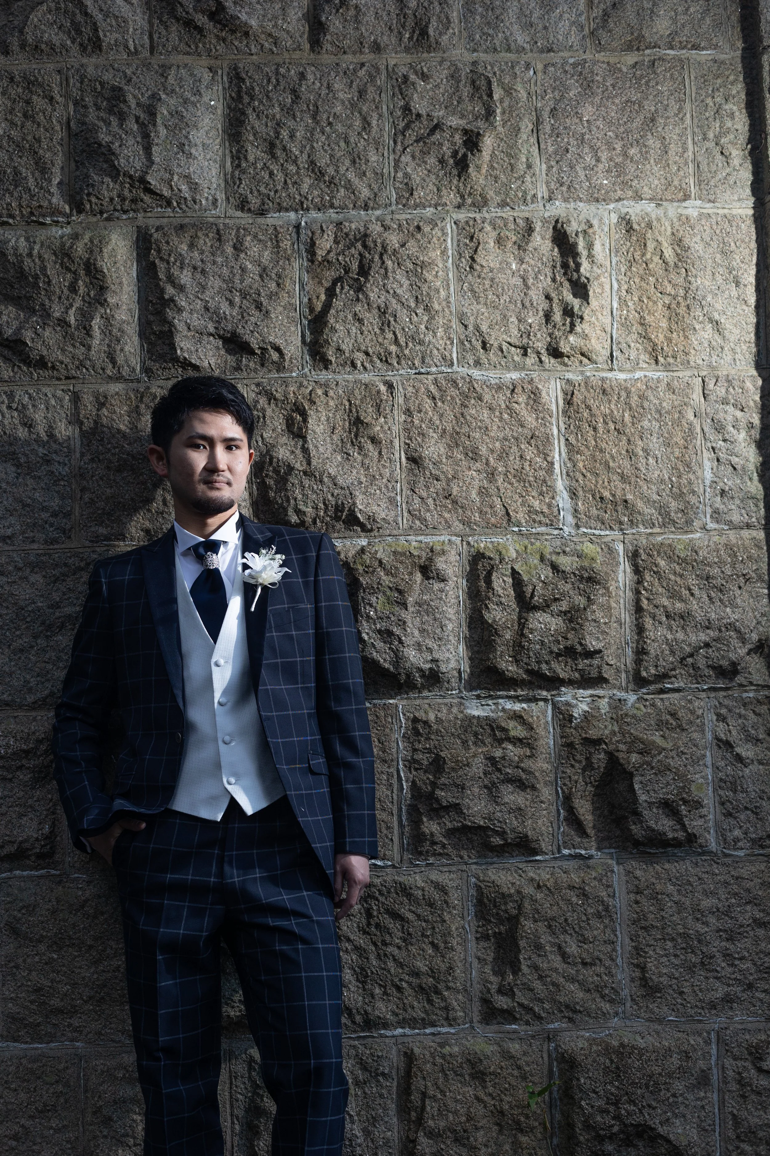 ロケ撮影イメージ | 江田島 三高山砲台跡 | 石の壁の前に立つ男性、黒いチェックのタキシードを着用