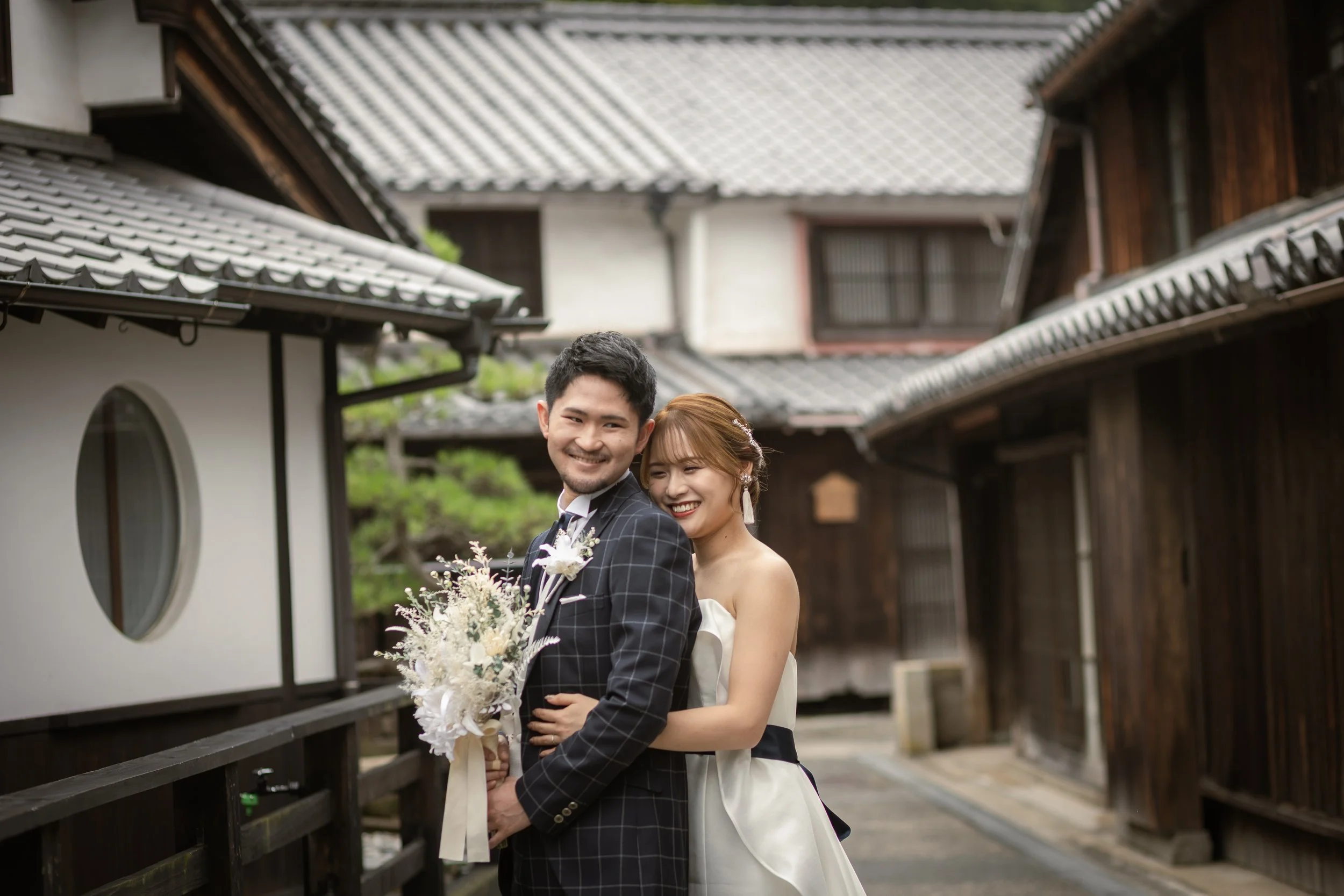 ロケ撮影イメージ | 御手洗町並み保存地区 | 結婚式をした新郎新婦が笑顔で並んでいる写真。背景は伝統的な日本家屋の街並み。