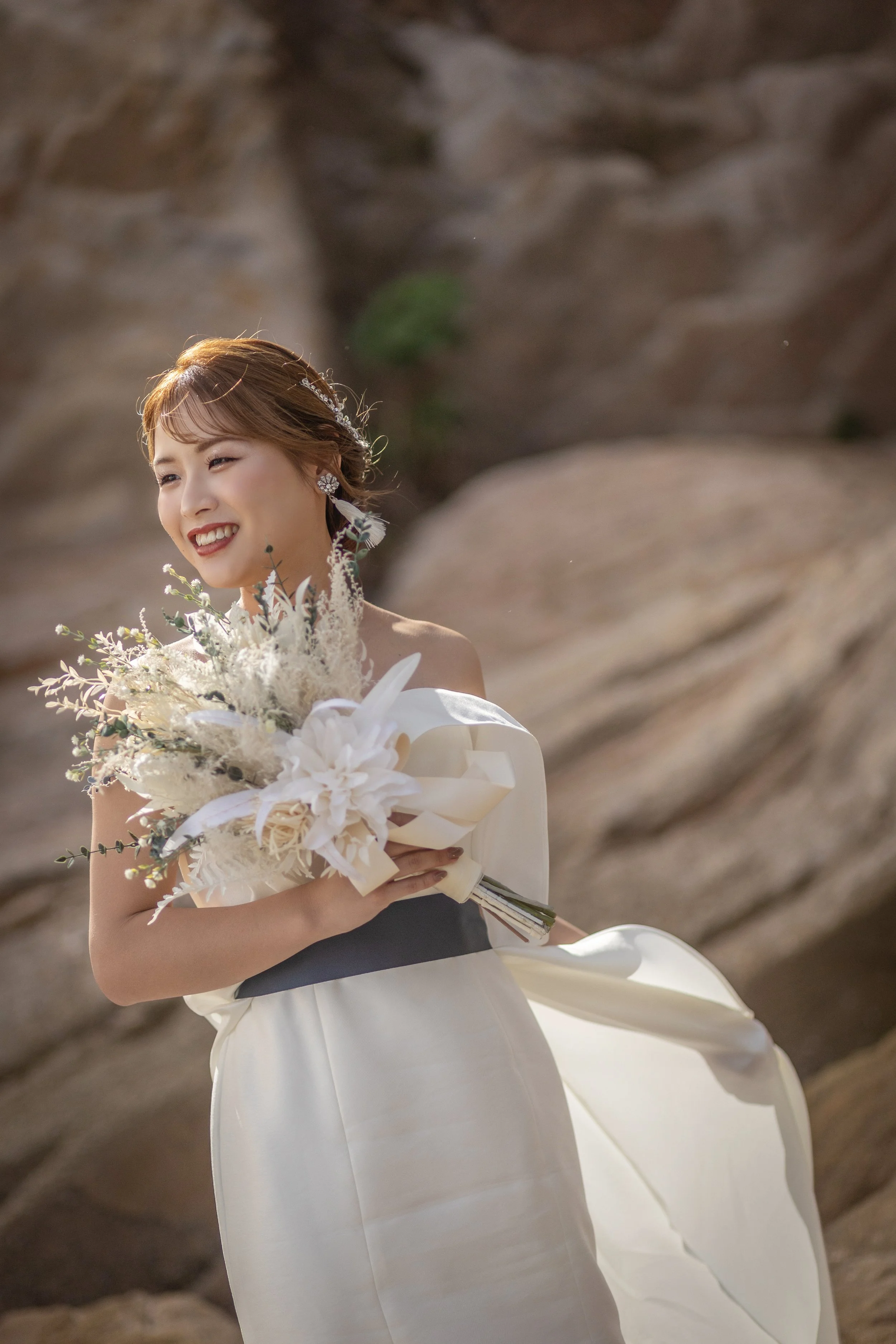 ロケ撮影イメージ | 江田島 入鹿海岸 | 結婚式の花嫁が笑顔で花束を持っている。背景は岩場の自然の風景。