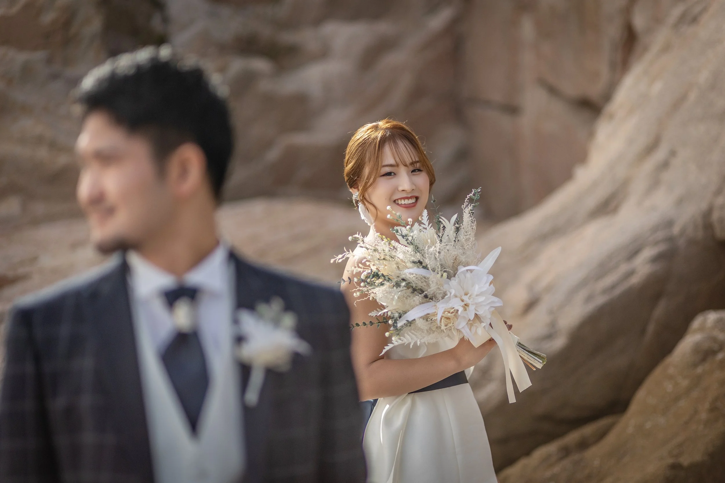 ロケ撮影イメージ | 江田島 入鹿海岸 | 結婚式の花嫁と花婿、花嫁は花束を持ち笑顔でポーズ、背景に岸壁。