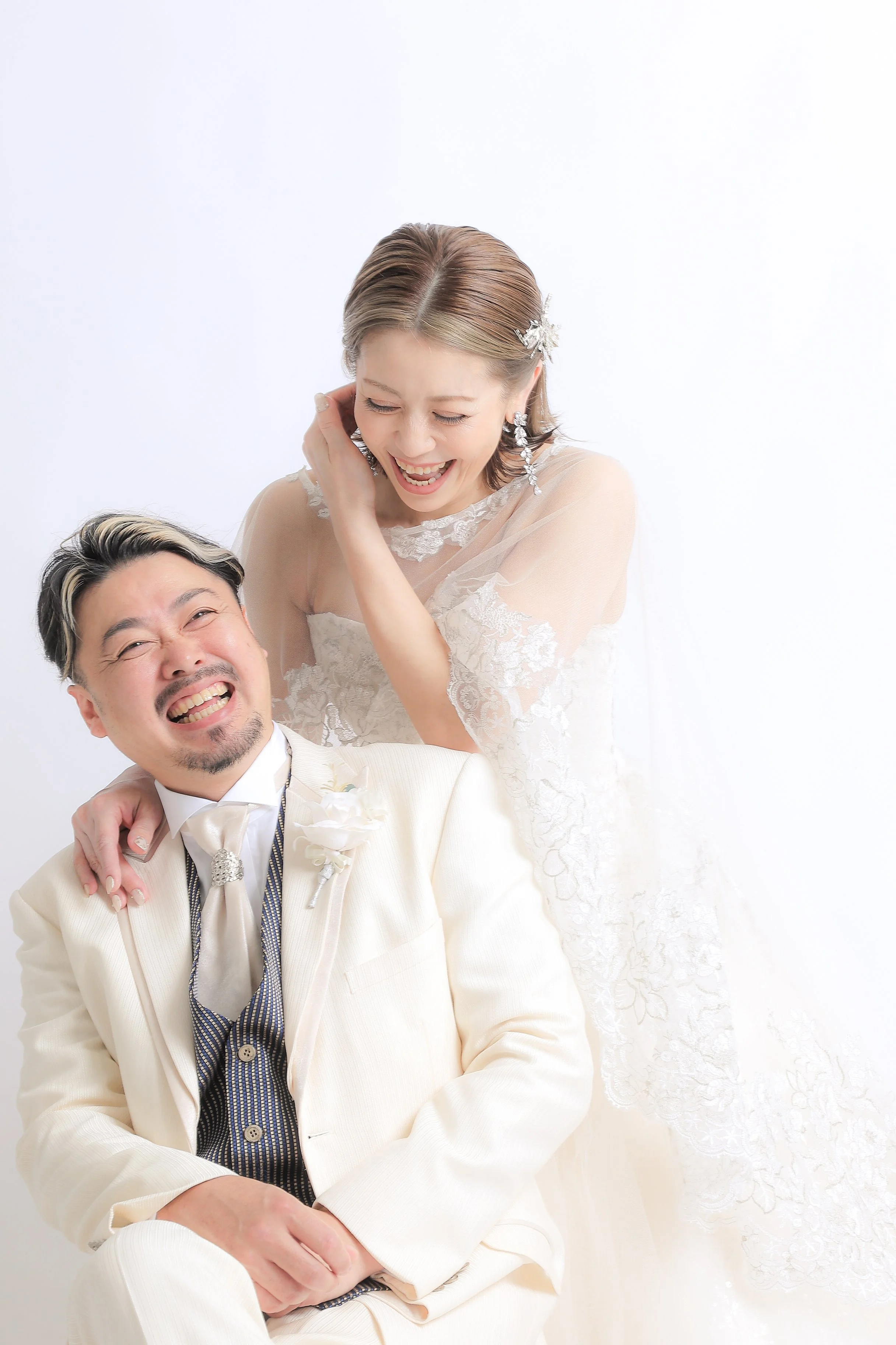 スタジオ撮影イメージ｜結婚式の花嫁と花婿の写真。二人とも笑顔で楽しそうにしている。花嫁は白いウェディングドレスを着ており、花婿は白いスーツを着ている。