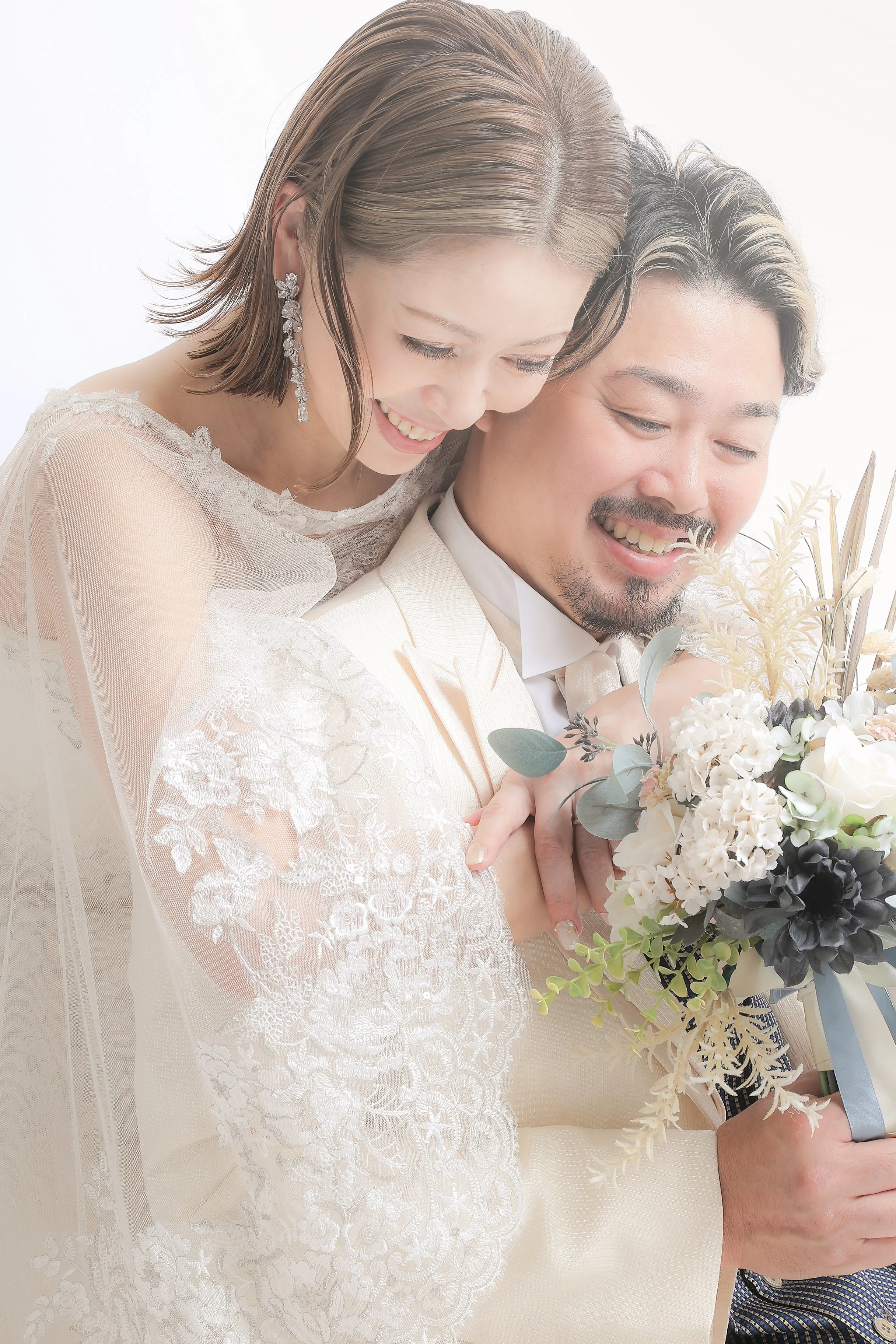 スタジオ撮影イメージ｜結婚式の夫婦がお互いを抱き合い笑顔で、花束を持っています。