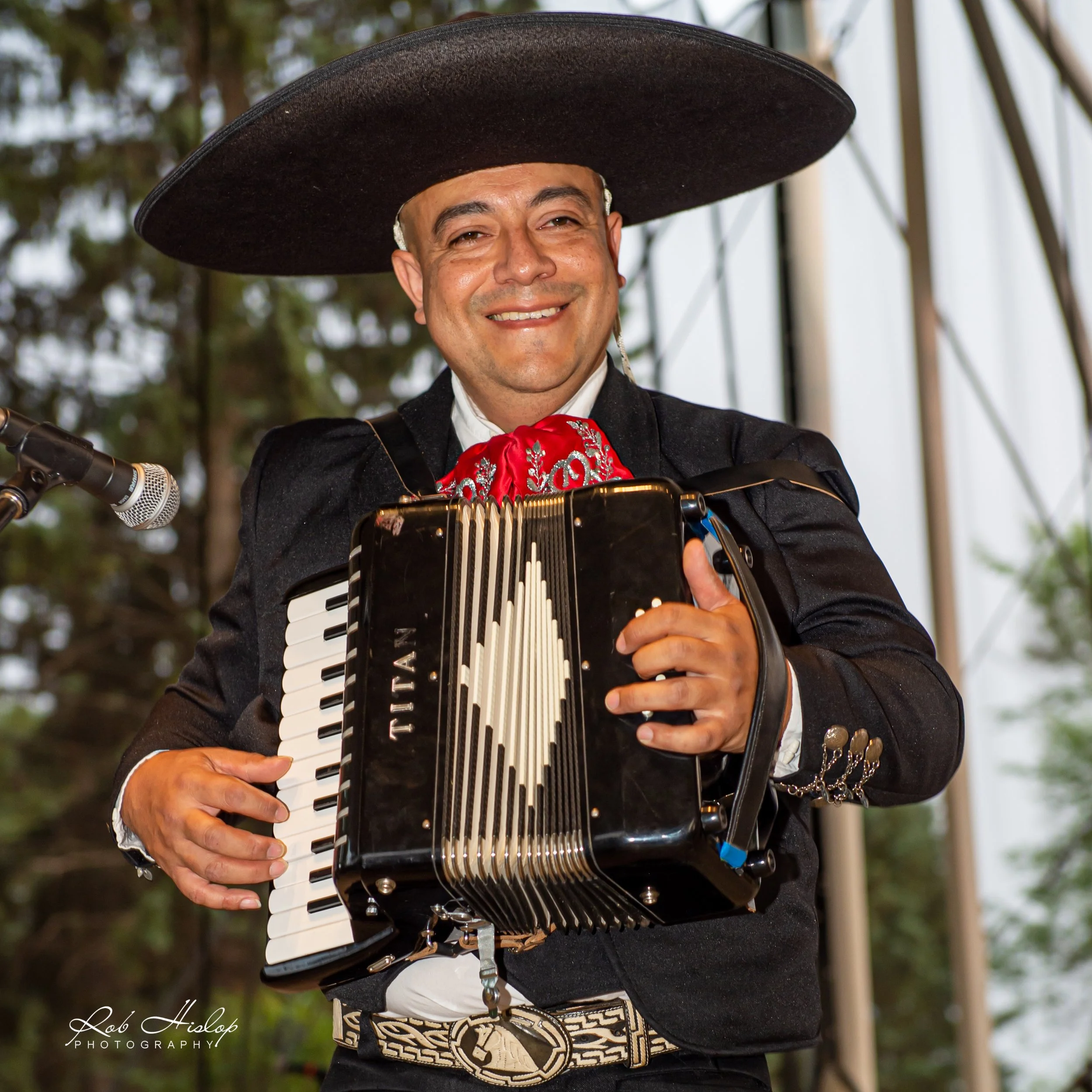 A man wearing a traditional Mexican hat and a charro suit playing an accordion.