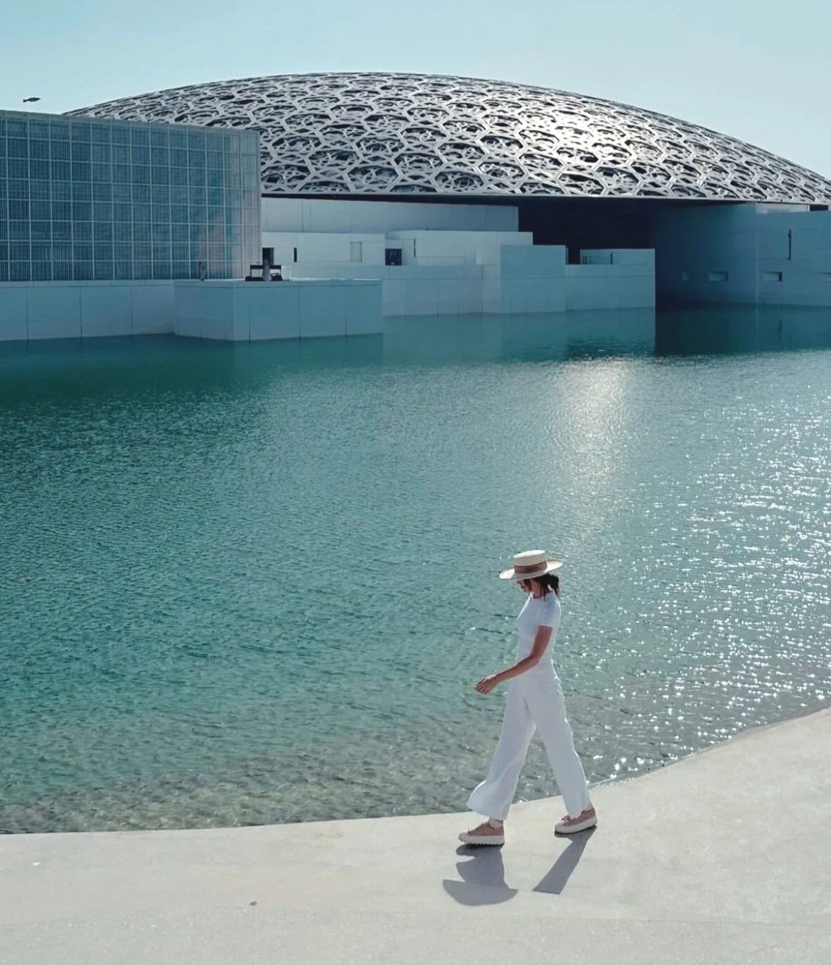 Person walking beside water with dome-shaped building in background