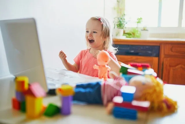 Child participating in remote online speech therapy on a laptop, smiling during a virtual speech-language therapy session at home.