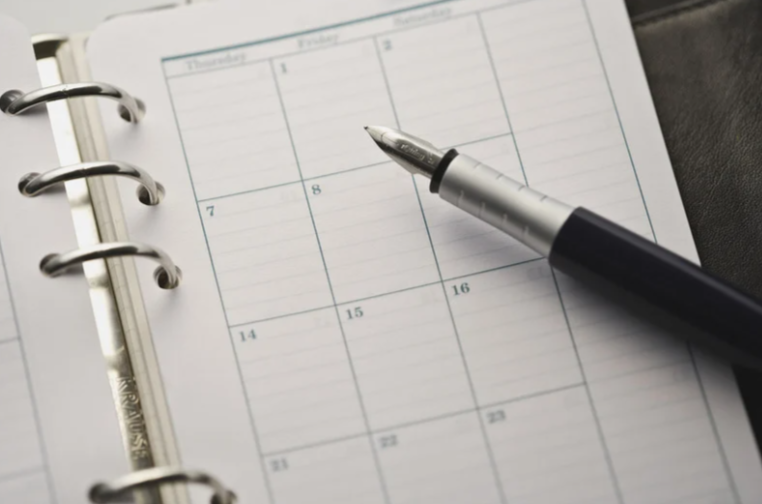 A blank weekly planner page with a black pen resting on it, seen from above.