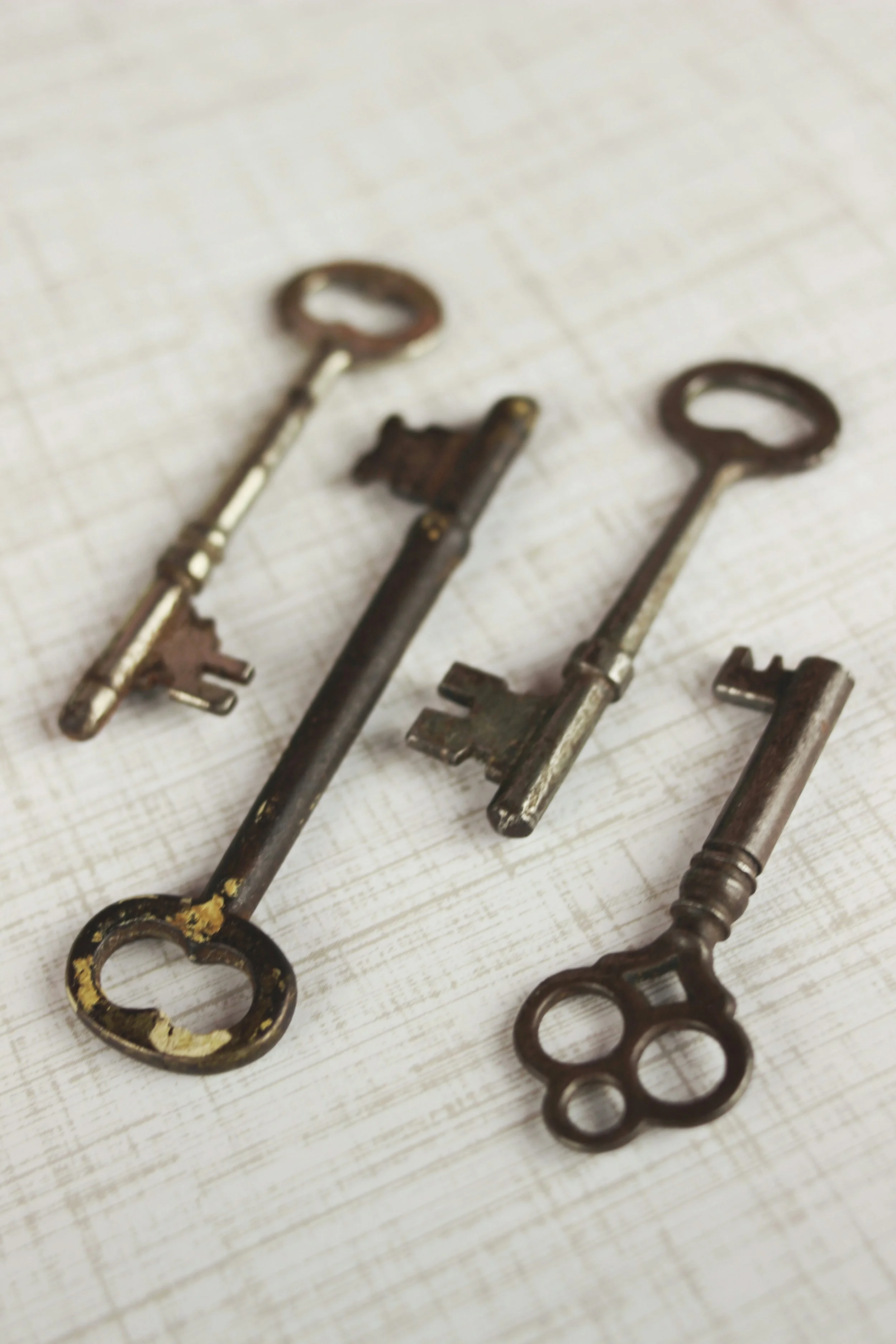 Four vintage keys, varying in size and design, laid on a light-colored wooden surface.