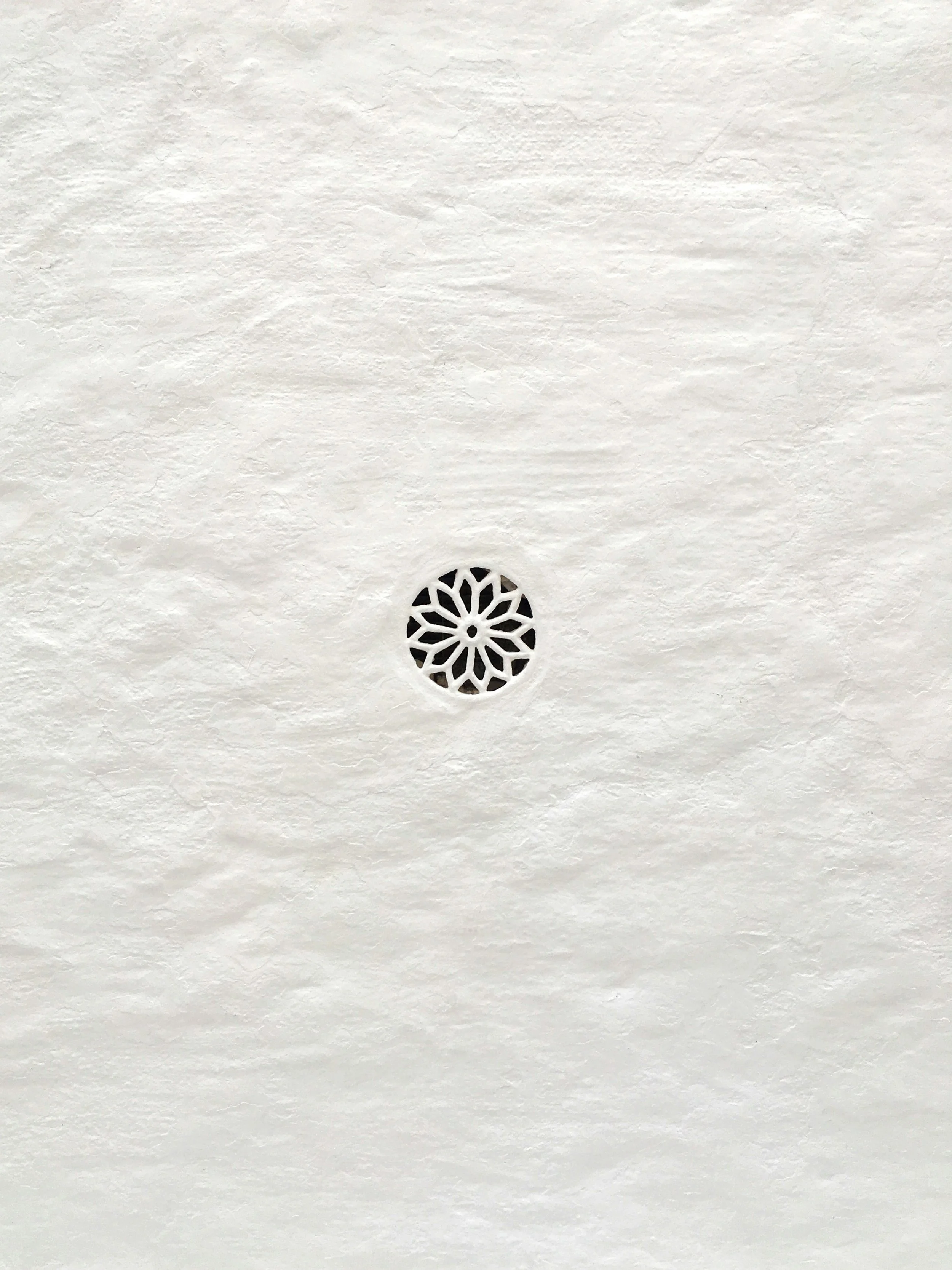 Close-up of a white textured ceiling with a small circular decorative vent.