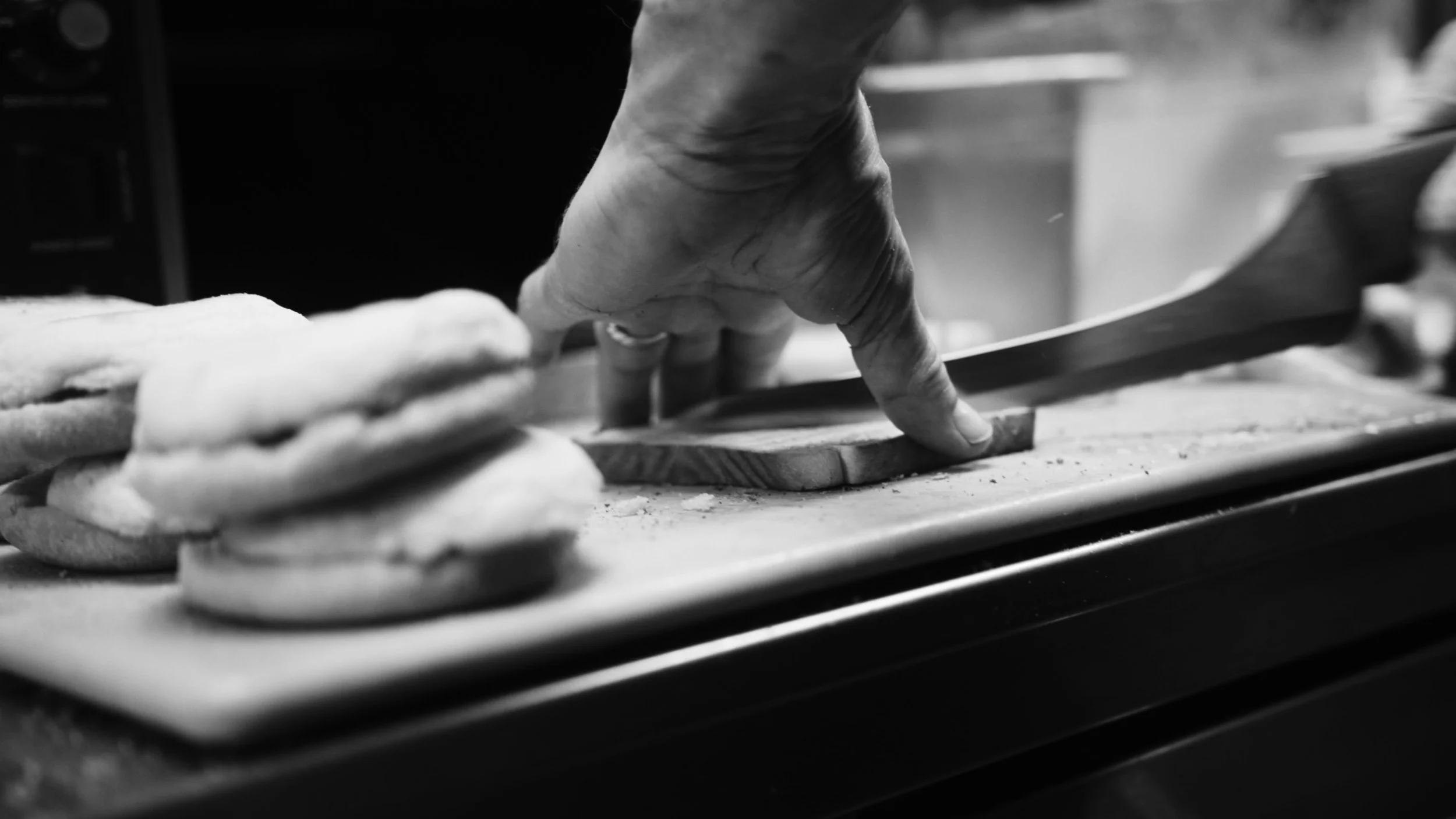 A person is slicing a piece of bread with a knife on a cutting board in a black-and-white photo.