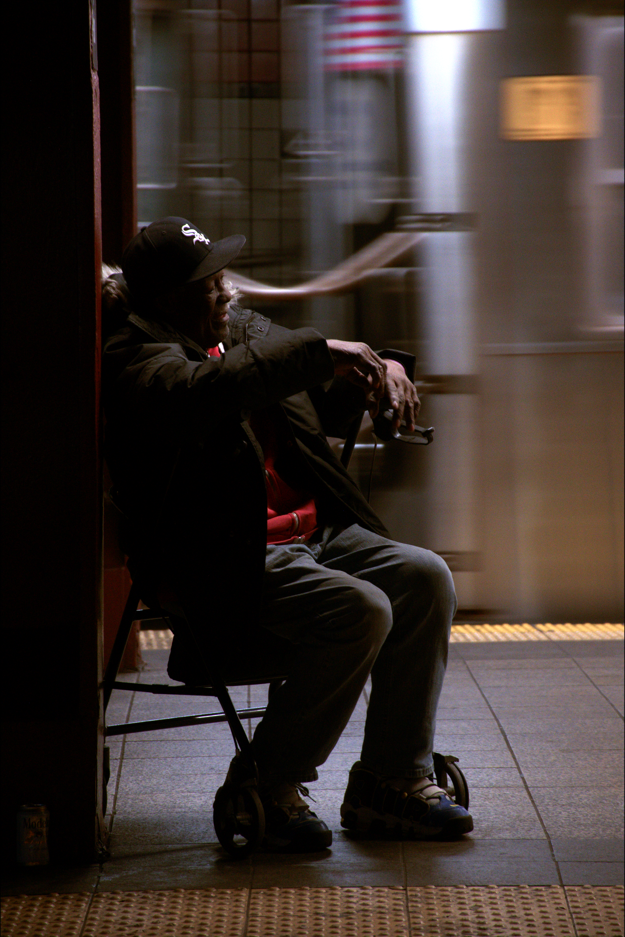A person sitting in a wheelchair and waiting at a subway station as a train passes by in the background.