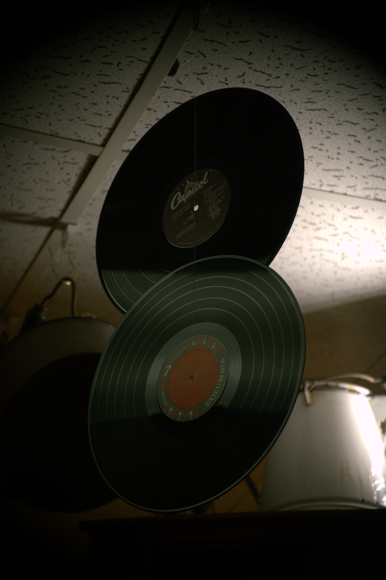 Vinyl records hanging from the ceiling with a textured ceiling in the background.