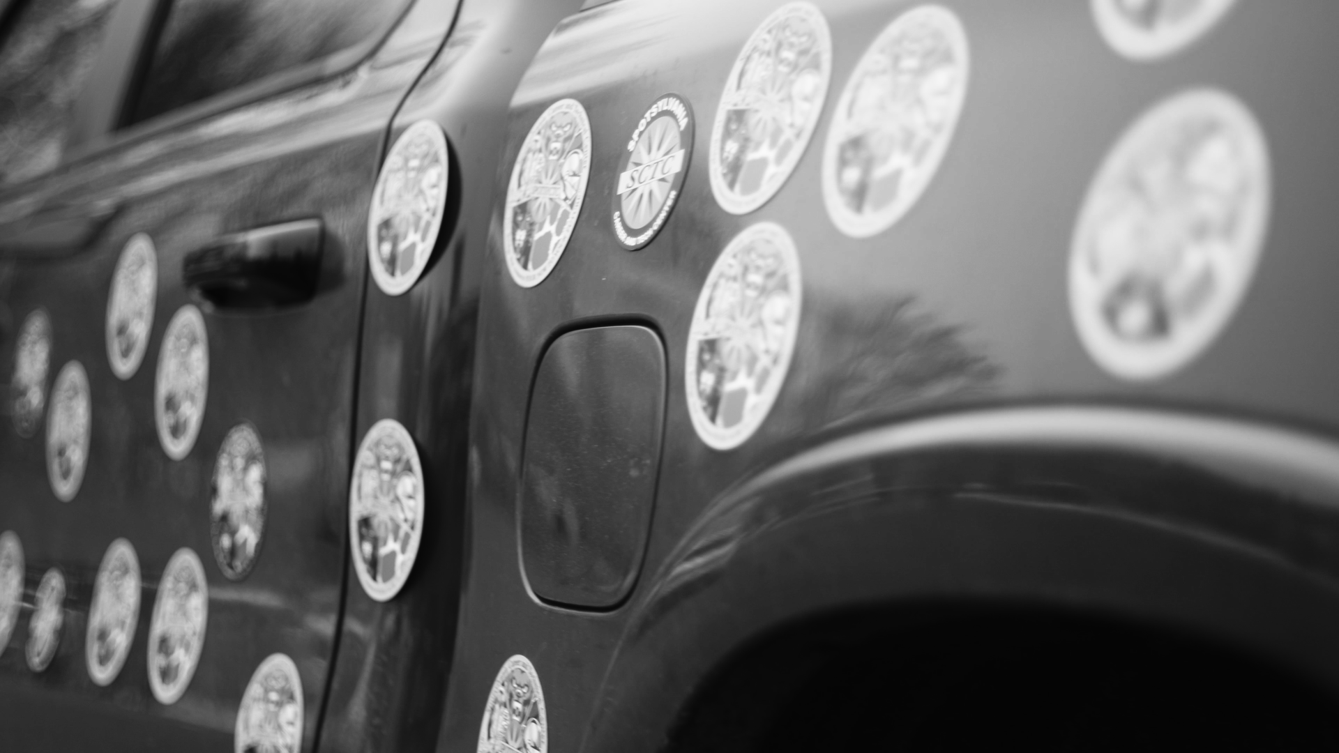 A close-up of a vehicle's side covered with multiple circular stickers, some with text and logos, in black and white.