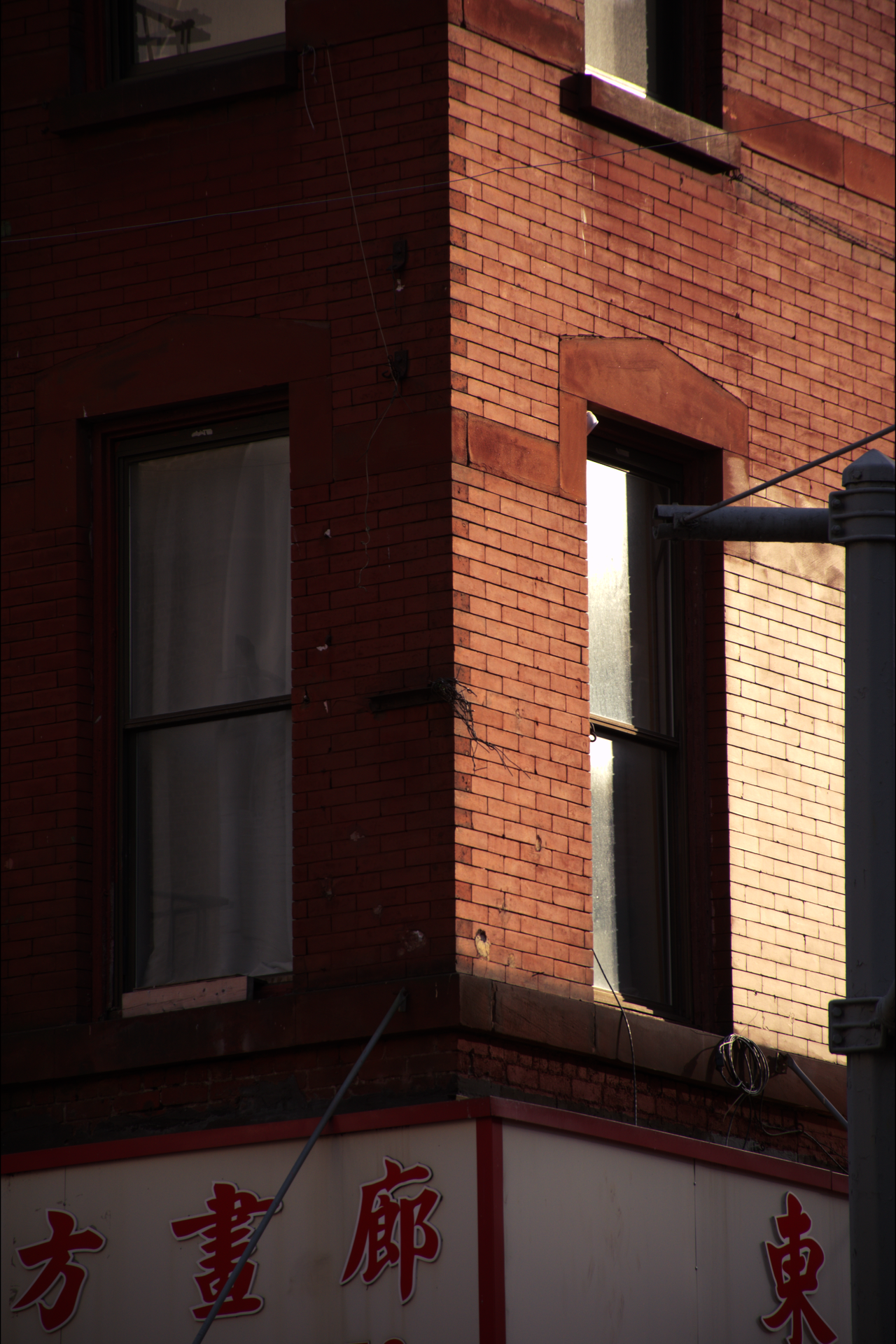 Close-up of a red brick building corner with window frames and a hanging wire at sunset.