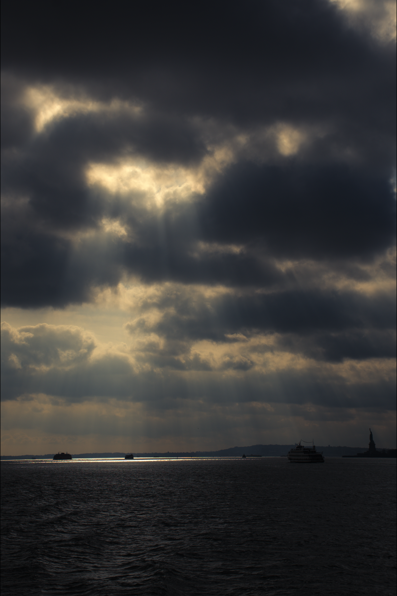 Dark stormy sky over water with boats and the Statue of Liberty in the distance.