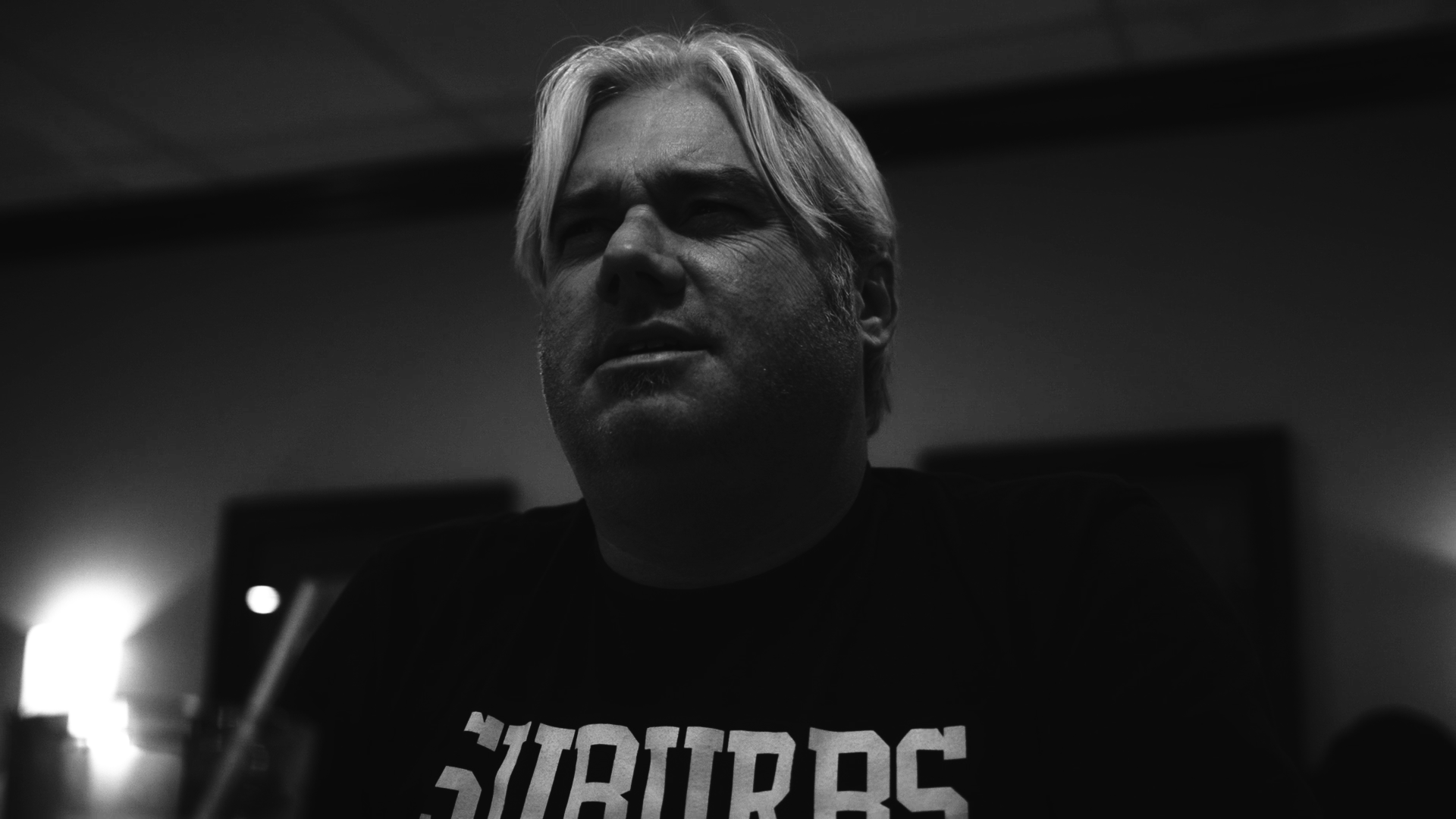 Black and white photo of a man with light-colored hair, looking to the side with a serious expression, indoors with soft lighting.