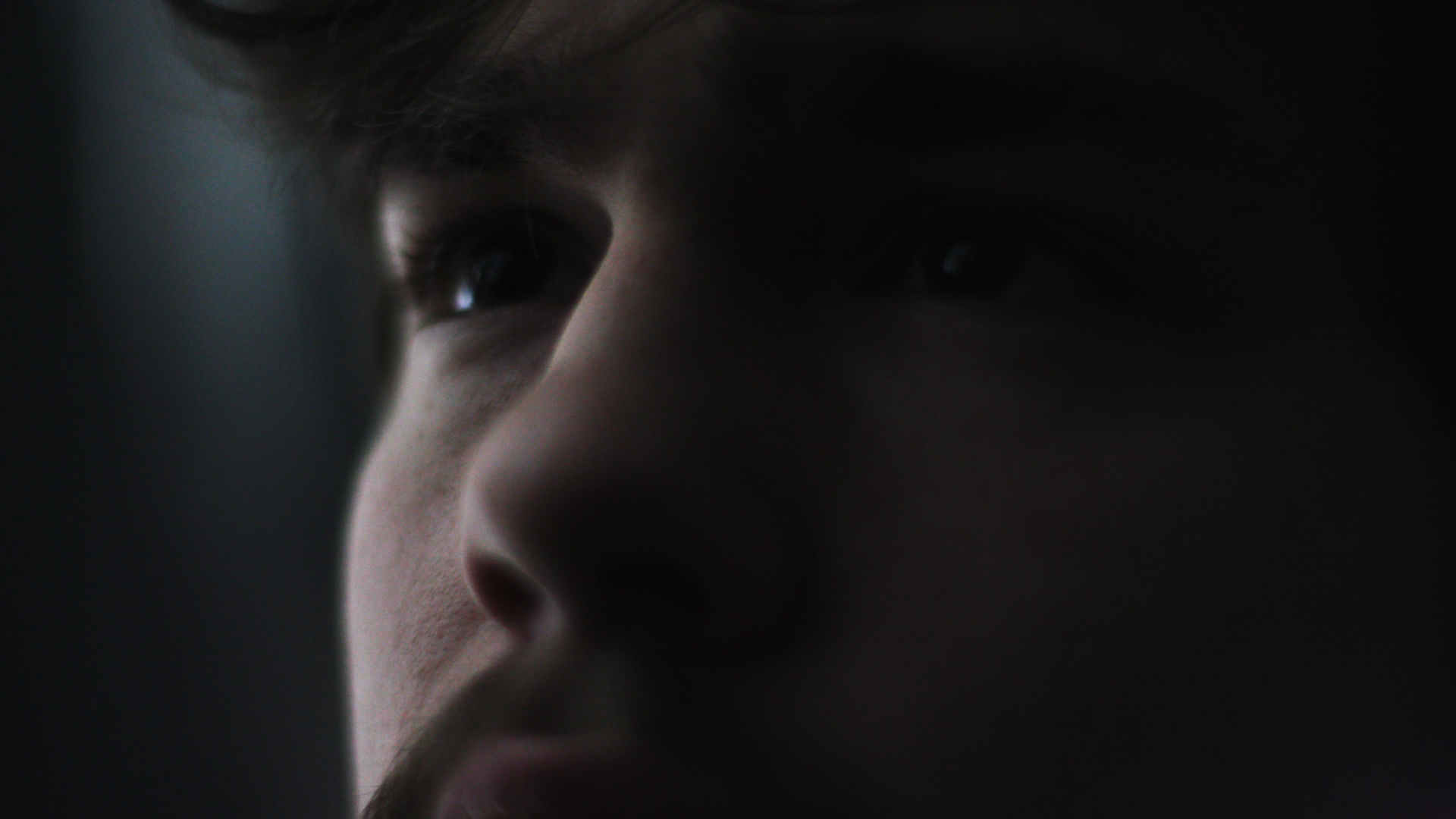 Close-up of a young man's face in low light, focusing on his eyes and nose.