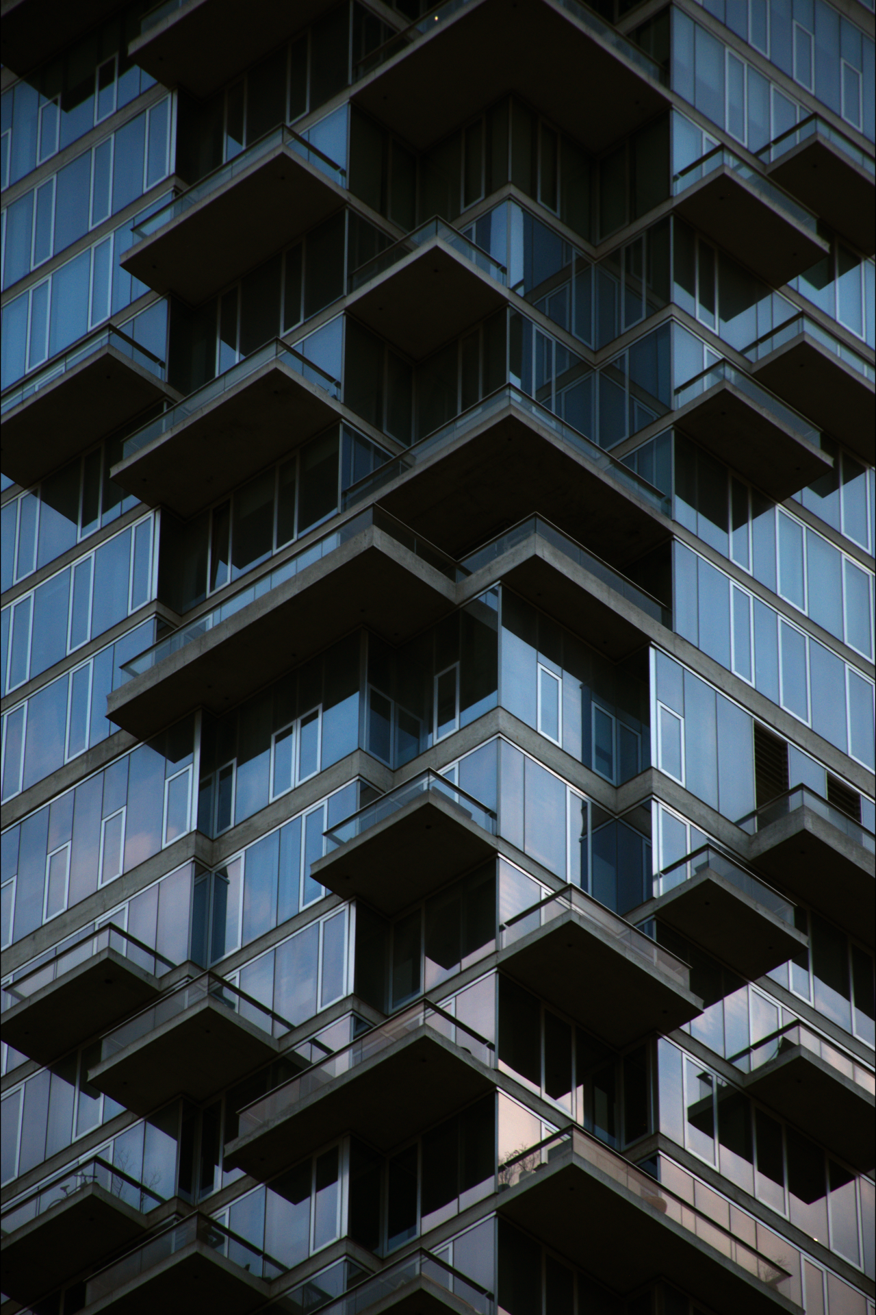 Close-up view of a modern high-rise apartment building with numerous glass balconies and reflective windows.